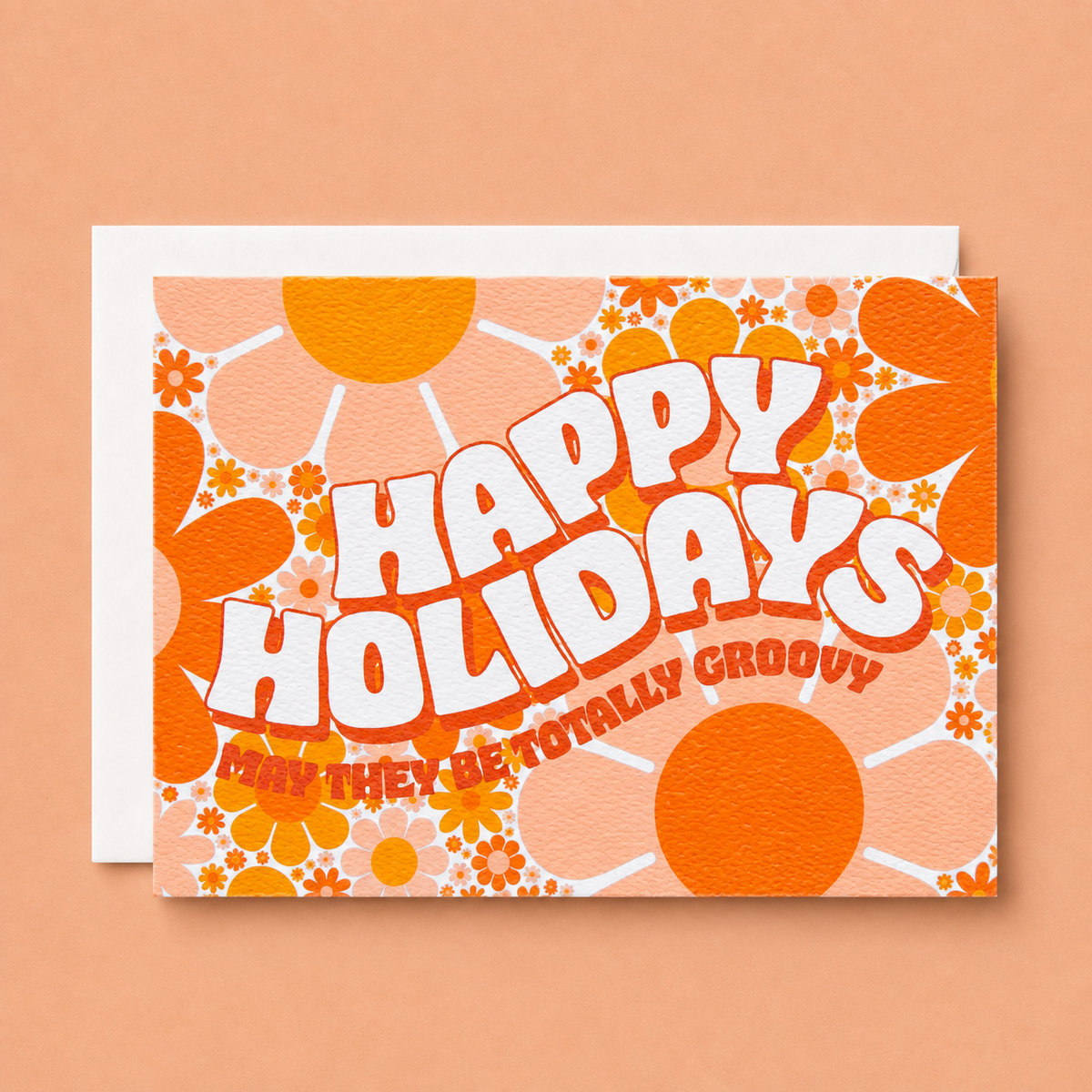 Card filled with a funky 70’s design made up of orange and peach daisies. On top of the design is white block lettering with a red shadow that reads ‘Happy Holidays.’ Under that in red block text it reads ‘may they be totally groovy.’ This card is accompanied by a white envelope.