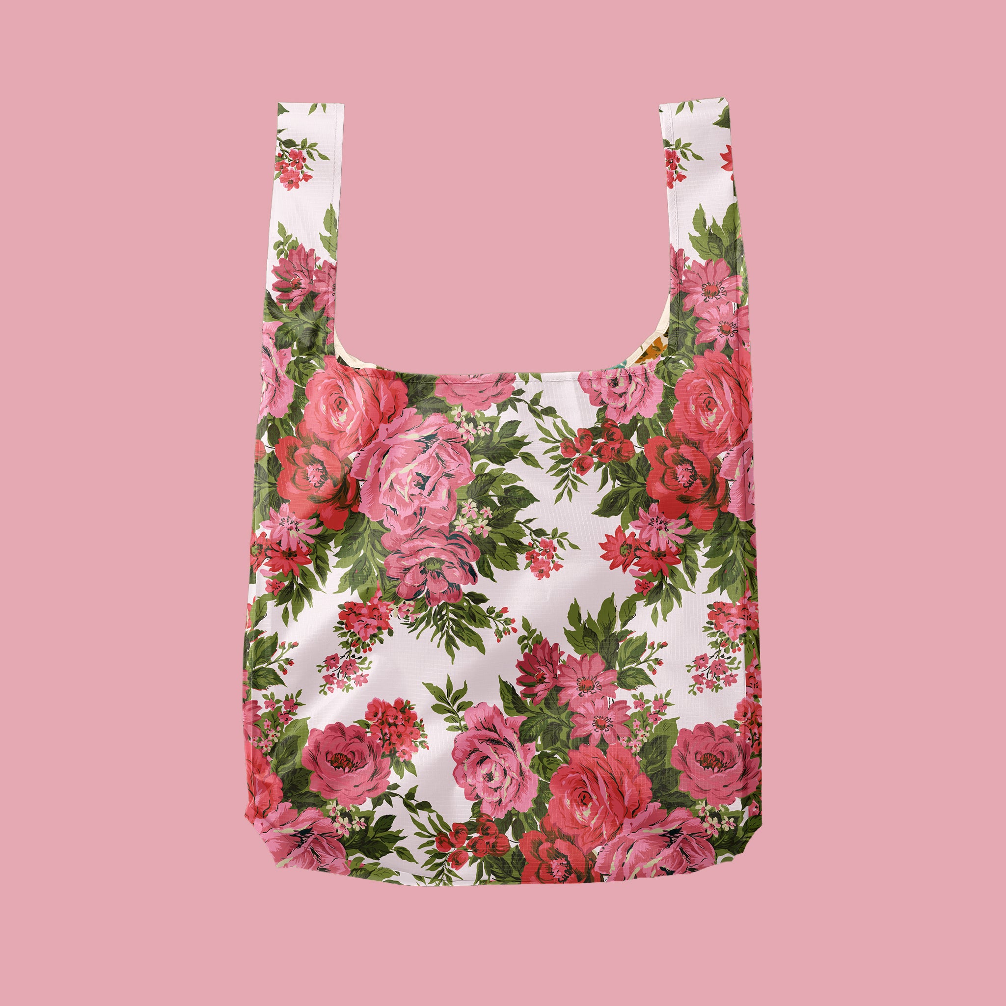 A reusable tote bag with a white background and beautiful pink and red roses and green leaves on a pink ground.