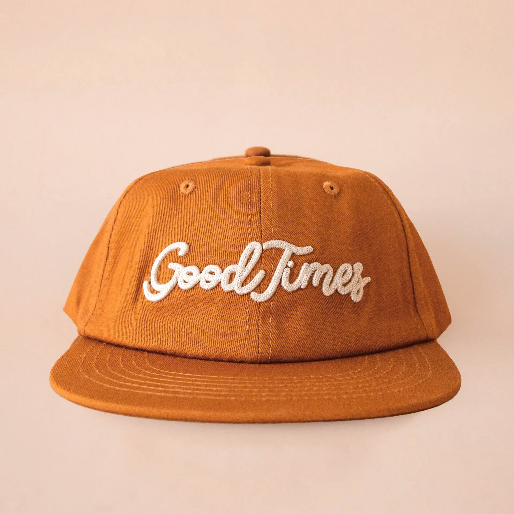 A burnt orange flat brim hat that reads, "Good Times" in ivory embroidered text.