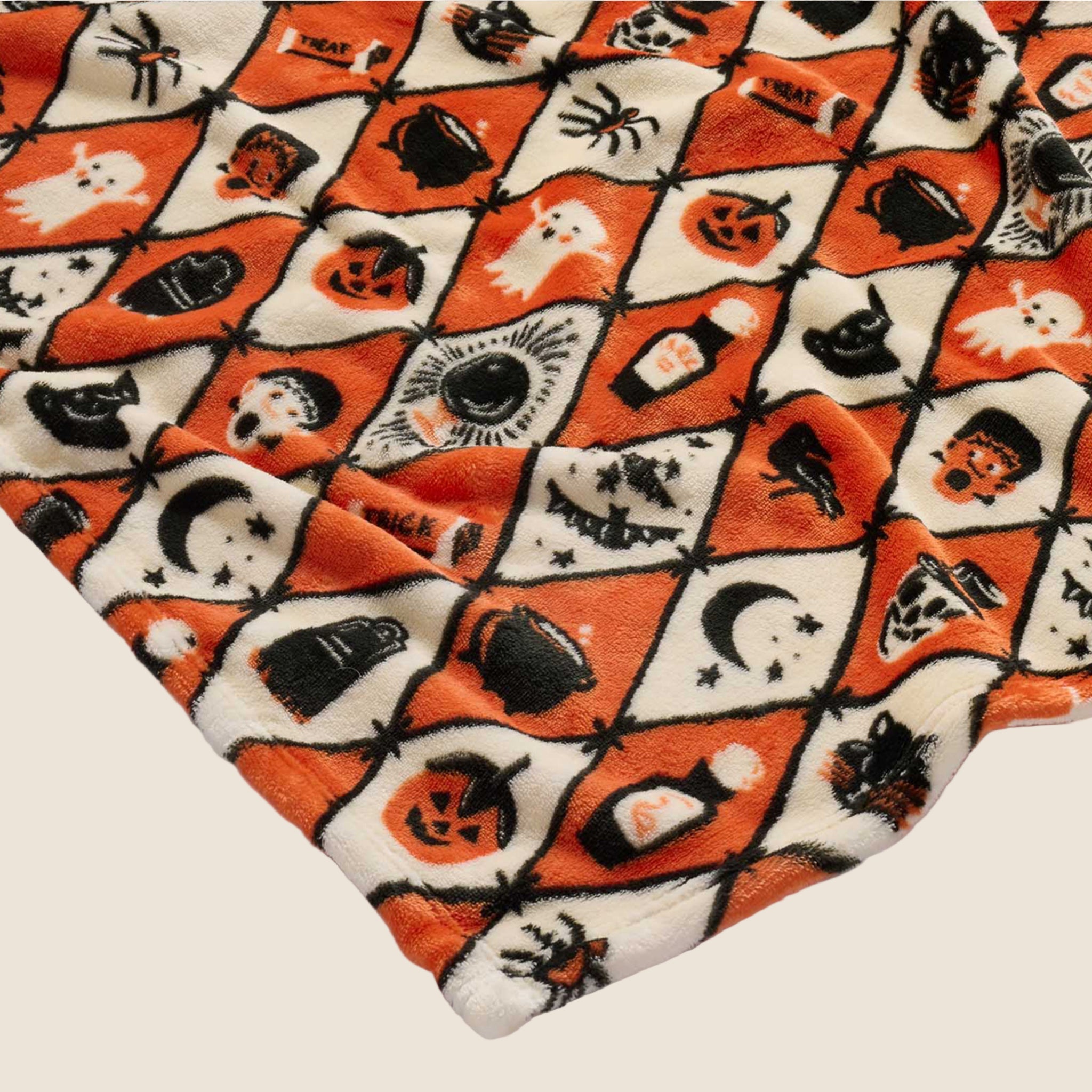 An orange, ivory and black diamond pattern fleece blanket with Halloween themed graphics. 