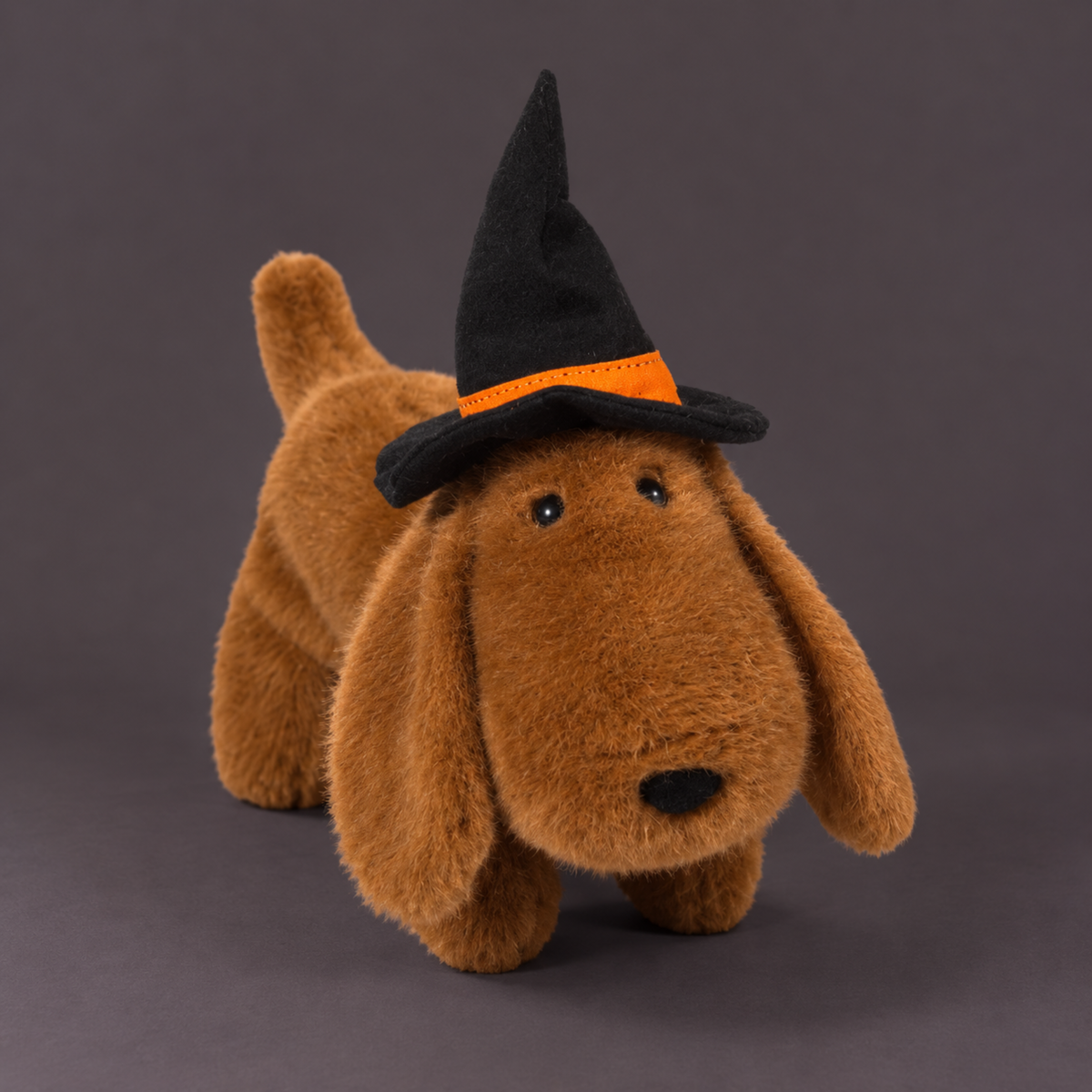 a brown dachshund plush toy wearing a black and orange witch hat.