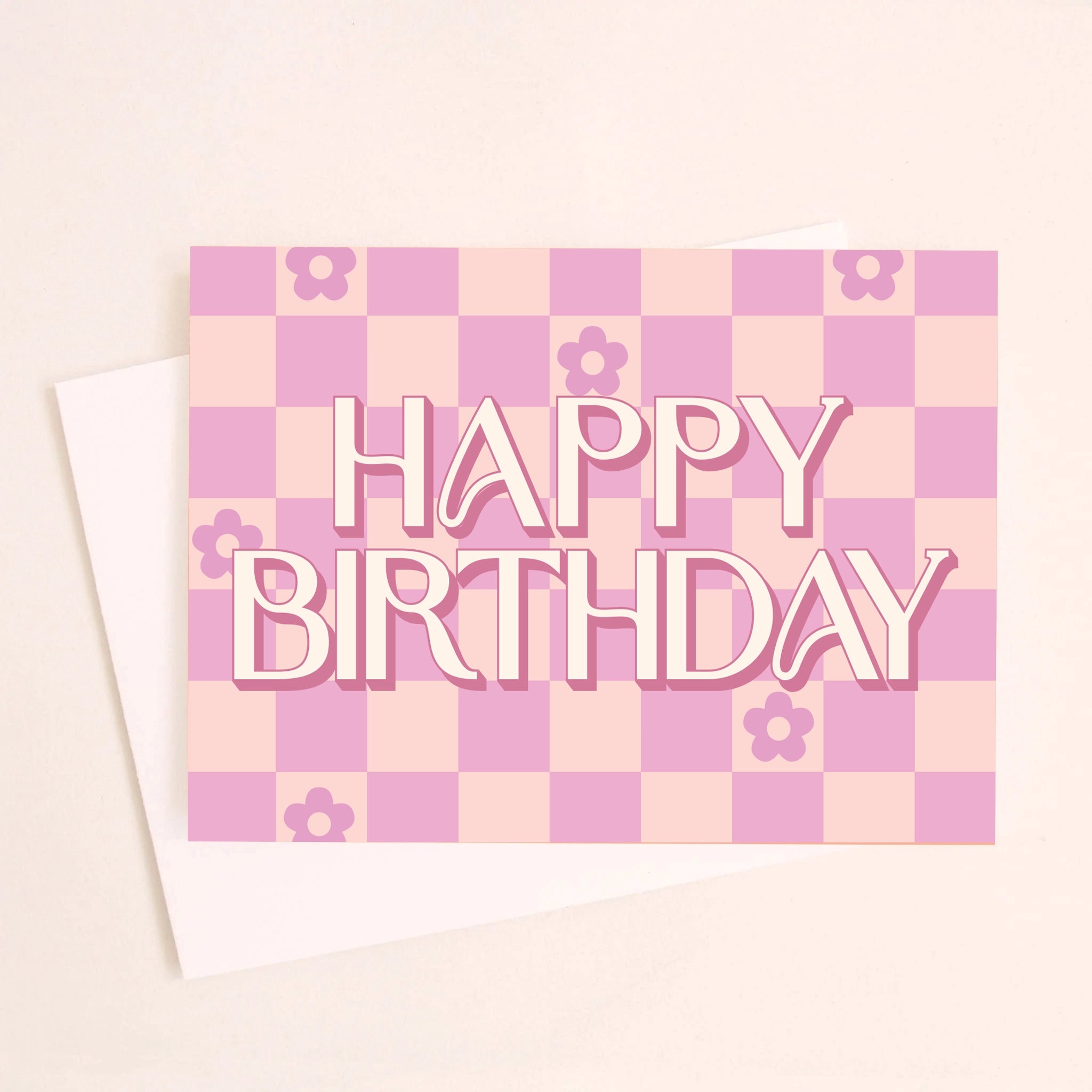 On a peachy background is a hot pink and light pink checkered greeting card with flowers in six of the checker squares along with text in the center that reads, &quot;Happy Birthday&quot;.
