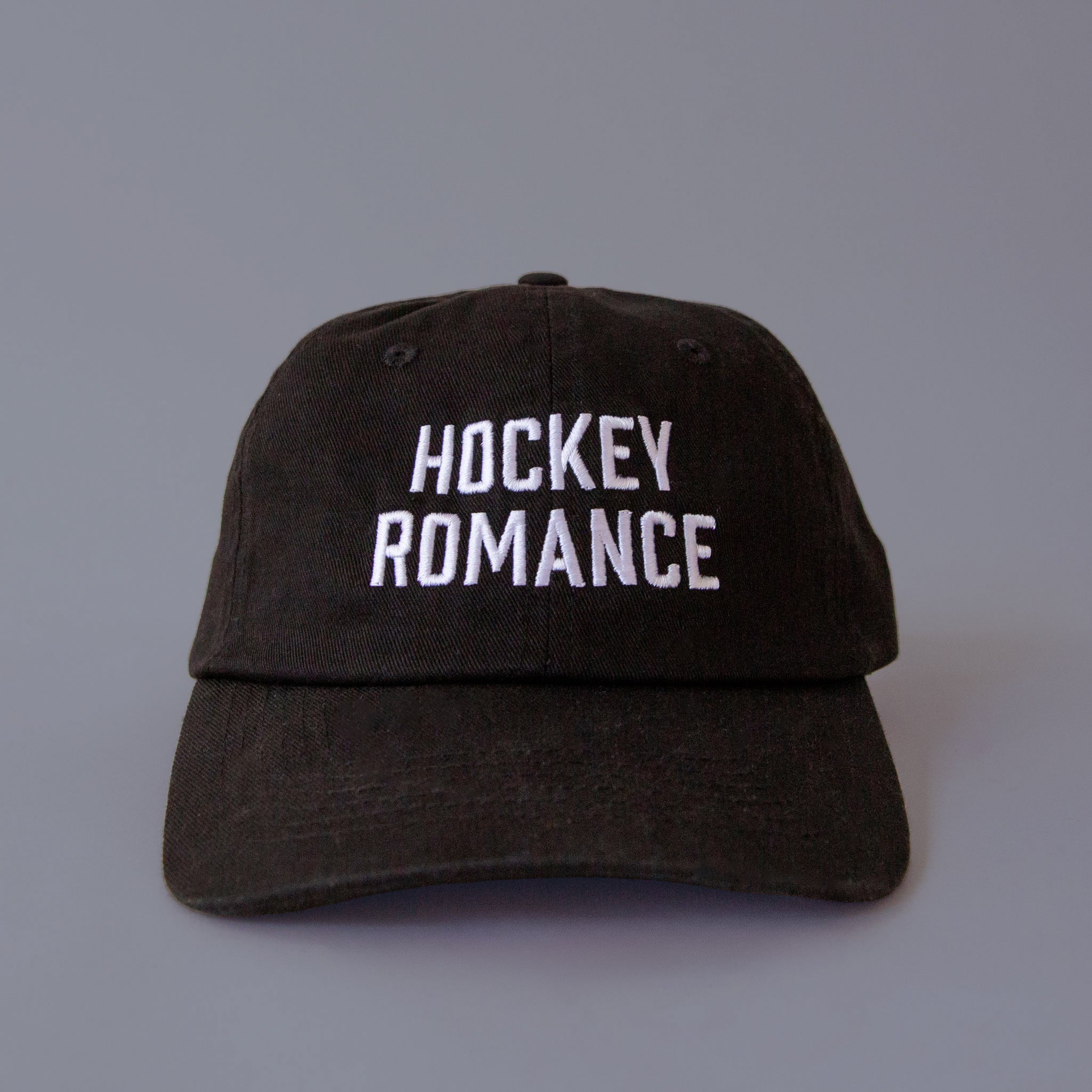 A black baseball cap with white embroidery that reads, "Hockey Romance". 