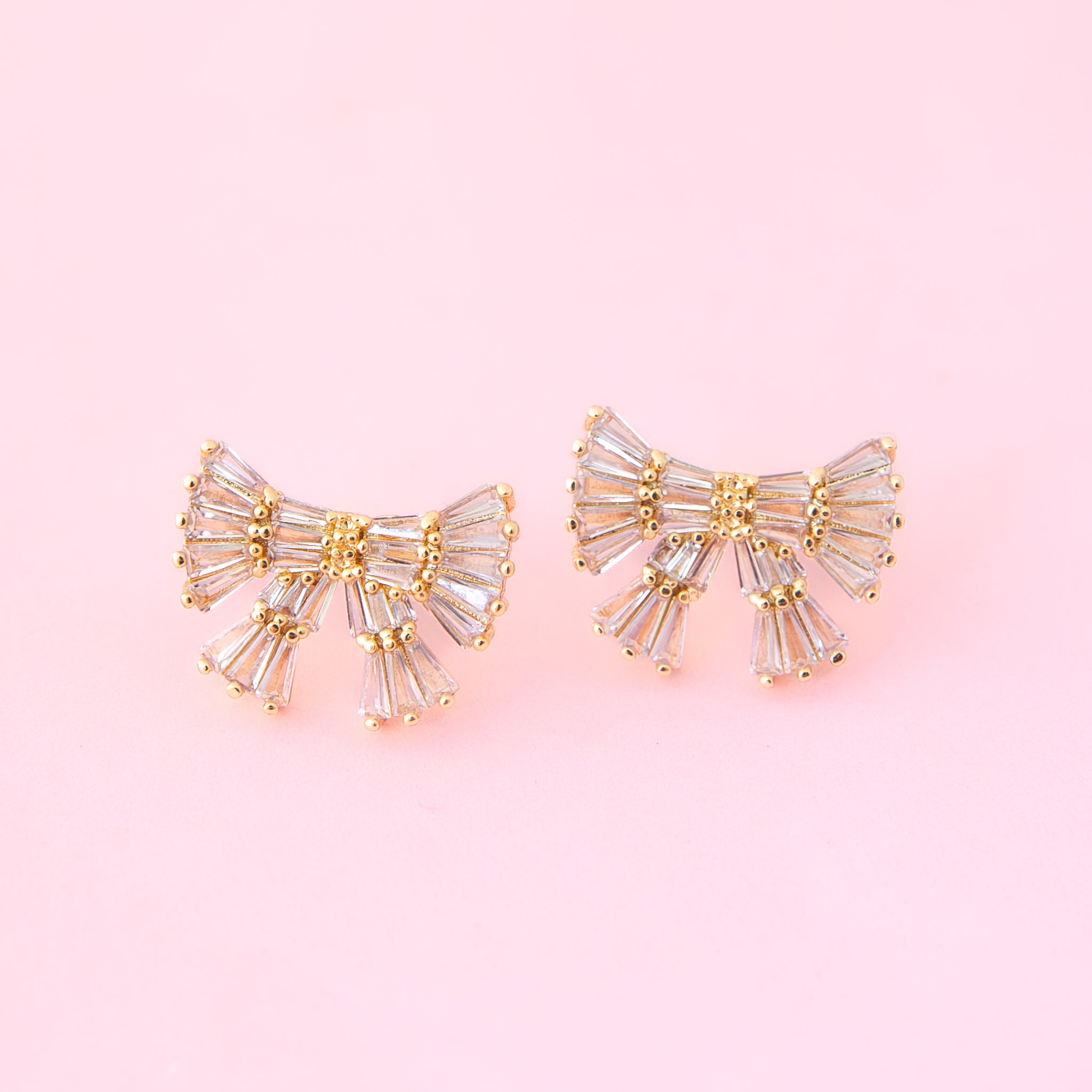 Gold and silver gemstone bow shaped earrings on a pink background.