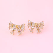 Gold and silver gemstone bow shaped earrings on a pink background.