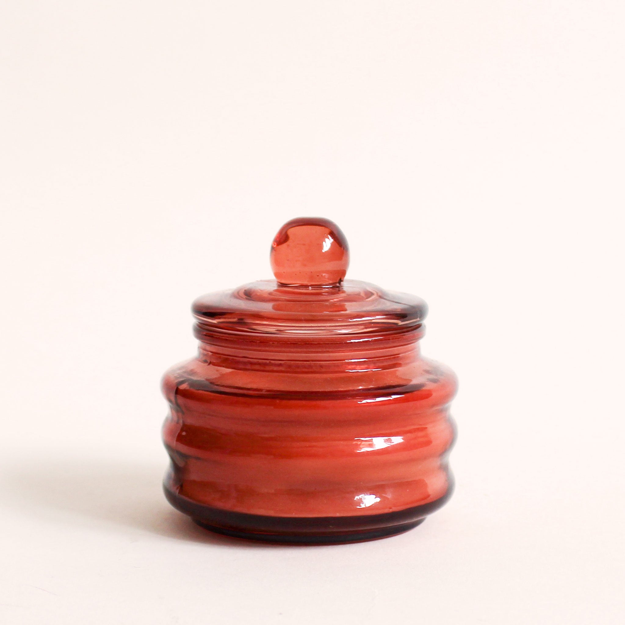 Red colored translucent beam candle vessel with white wax candle, and matching glass lid.