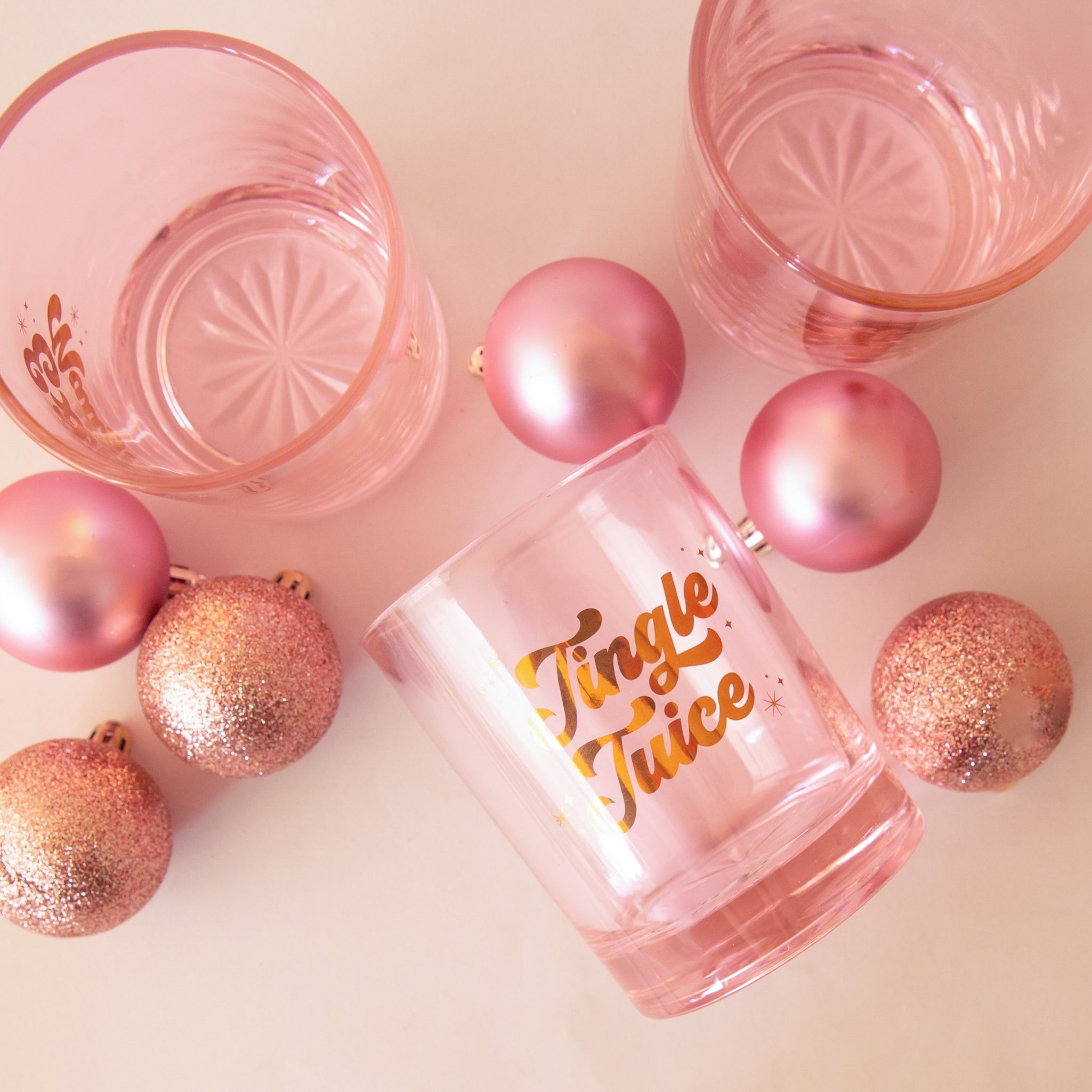 Glass cup with gold lettering is shown against a pink background that reads, &#39;Jingle Juice&#39;. 