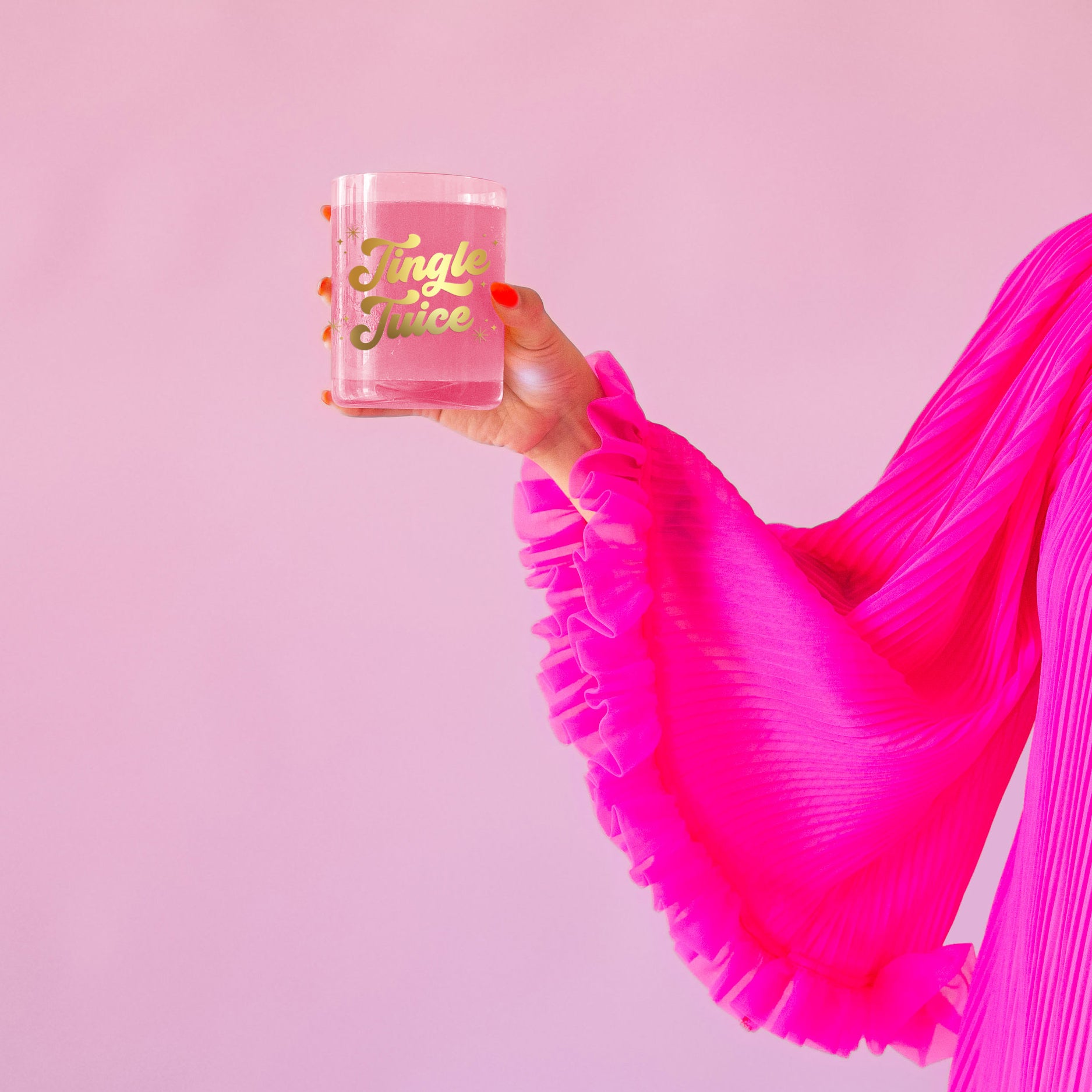 Glass cup with gold lettering is shown against a pink background that reads, 'Jingle Juice'. 