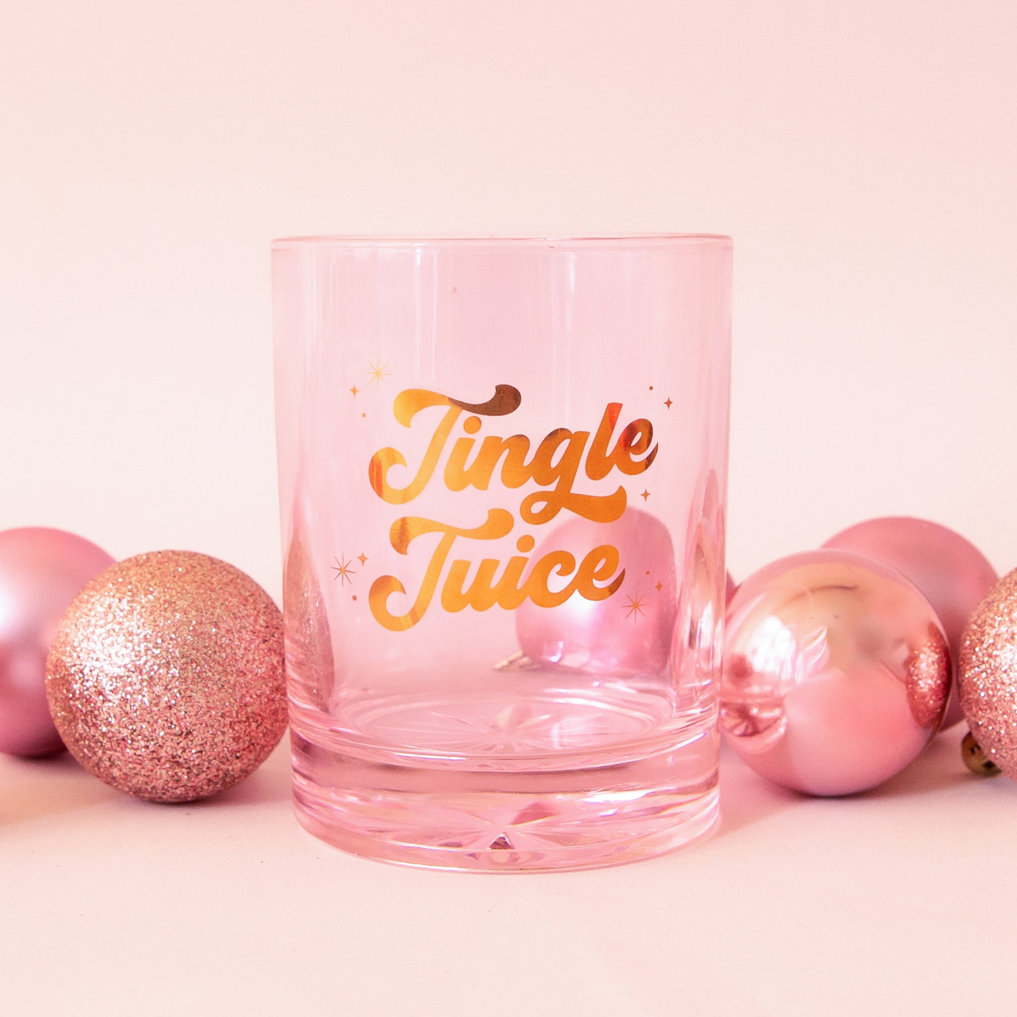Glass cup with gold lettering is shown against a pink background that reads, 'Jingle Juice'. 