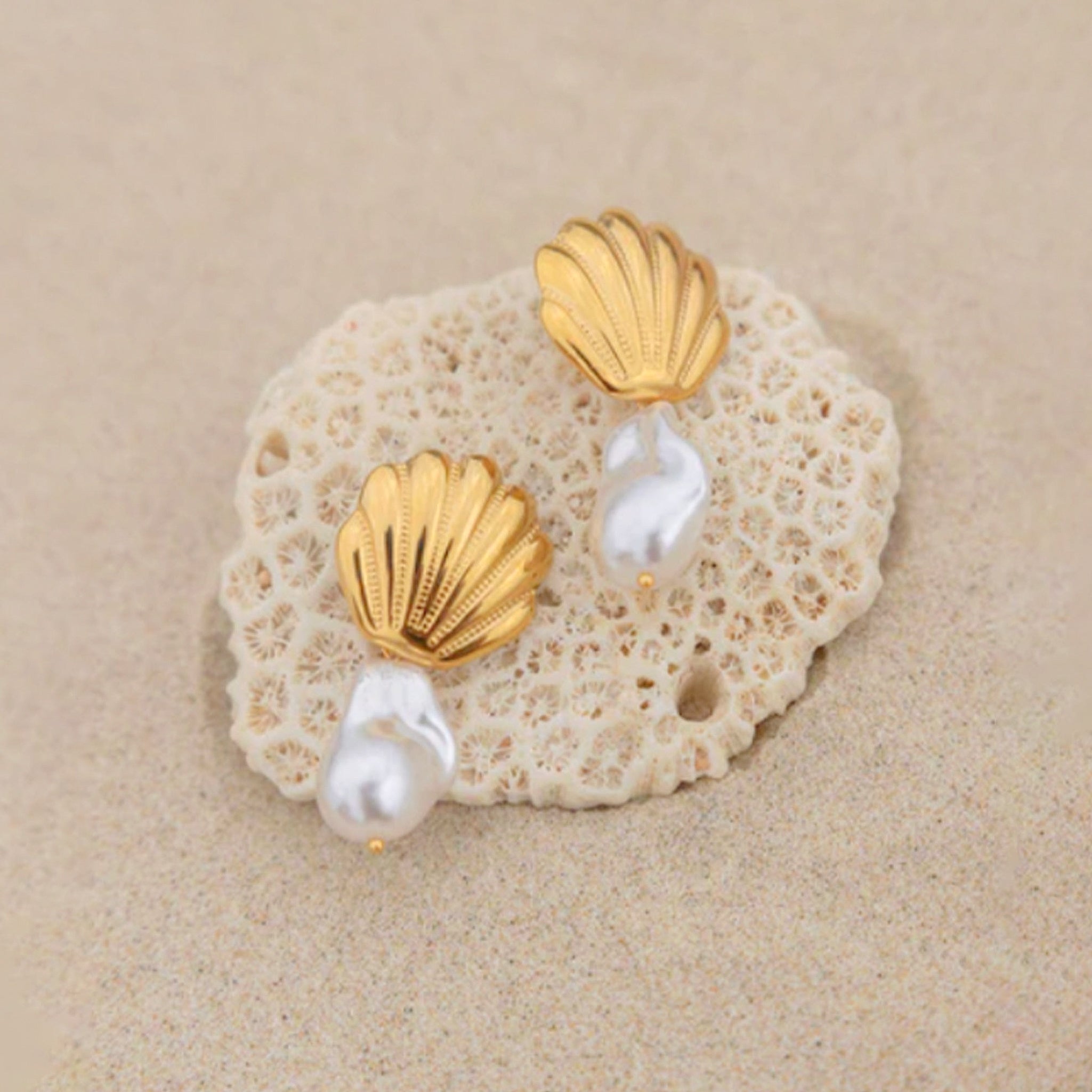 A pair of gold shell earrings with pearl beads underneath them. 