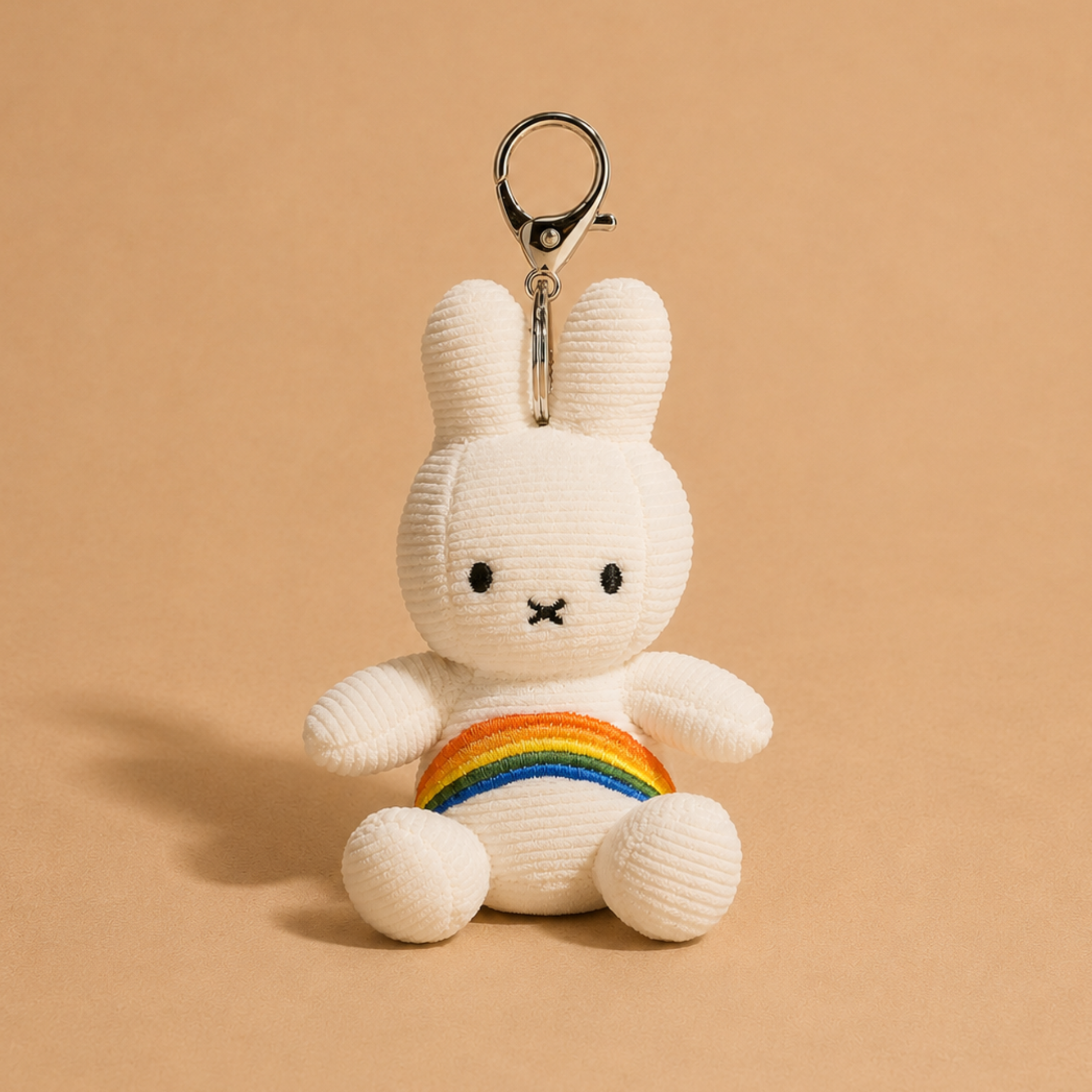 a white keychain with a plush miffy character with a rainbow design on its stomach. 