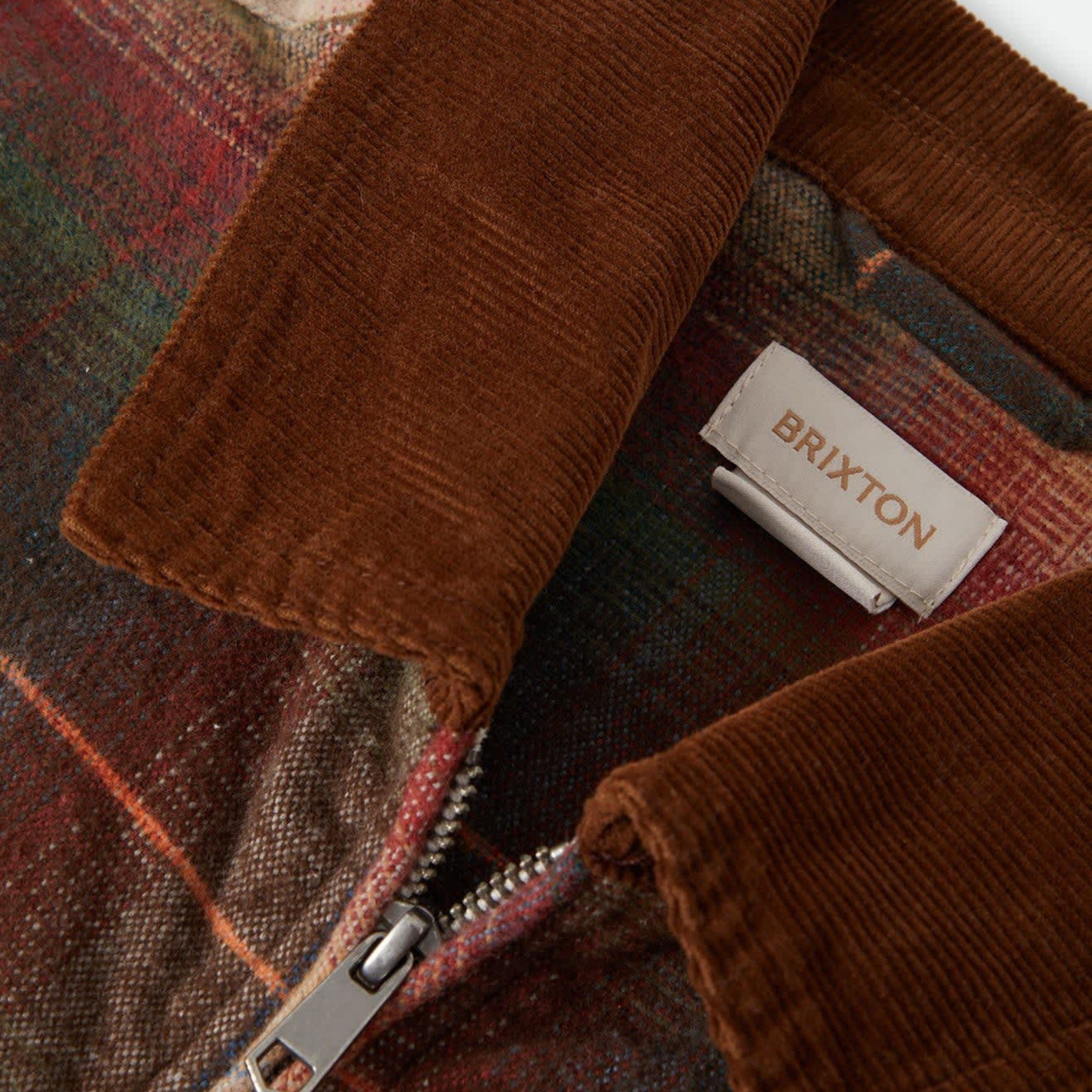 a multi colored zip up mechanics jacket with a brown corduroy collar. 
