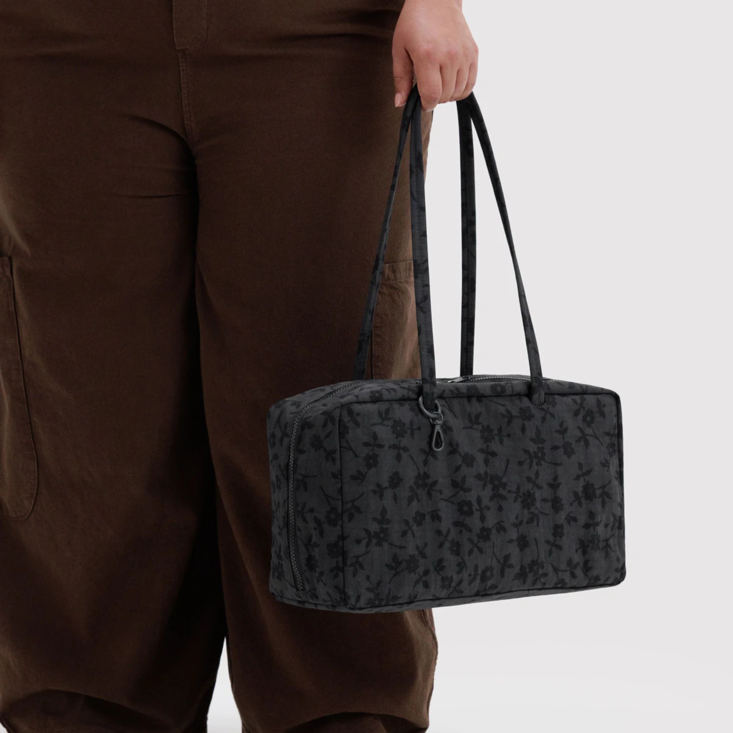 A black rectangular tote bag with a subtle floral pattern, featuring dual top handles and a top zipper closure