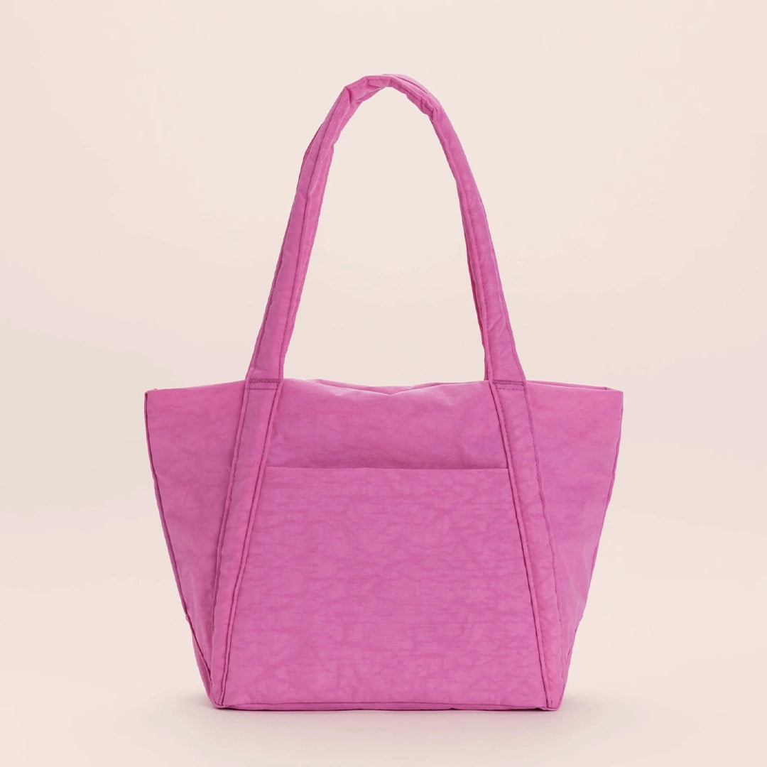 On a tan background is a bright pink tote bag made of durable nylon fabric with two large handles for over the shoulder and an outside pocket. 