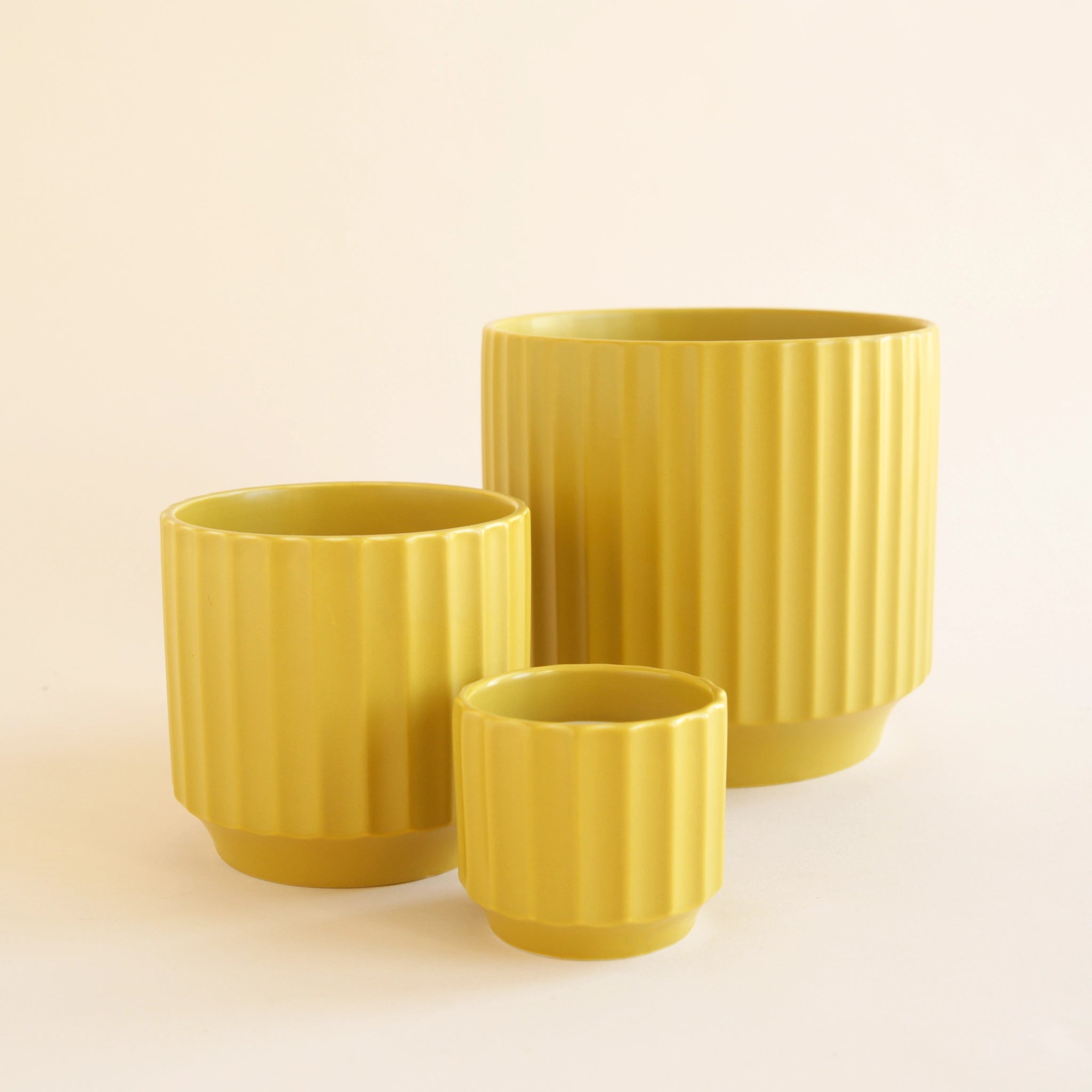 On an ivory background is three different sized charteuese ceramic pots with a ribbed texture around the sides.