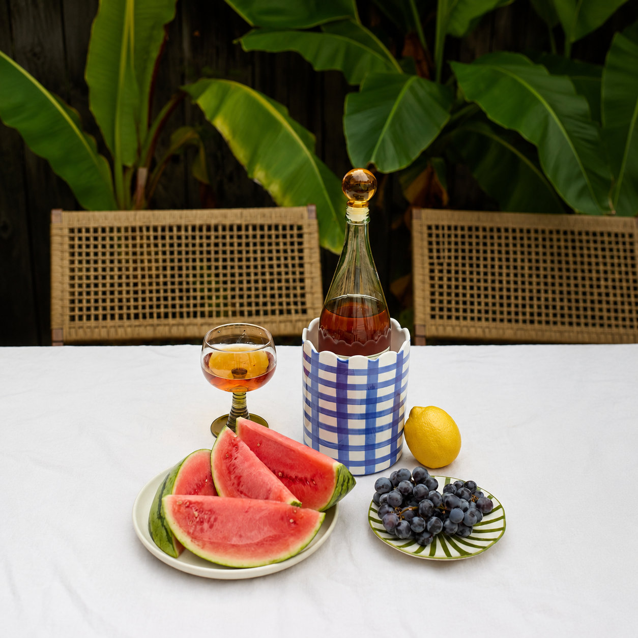 A table with slices of watermelon and blueberries on plates and a bottle of wine in a blue and white container.
