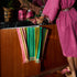 Styled bathroom vanity with a striped hand towel in pink, green, and olive draped over a wooden cabinet, surrounded by colorful accessories.
