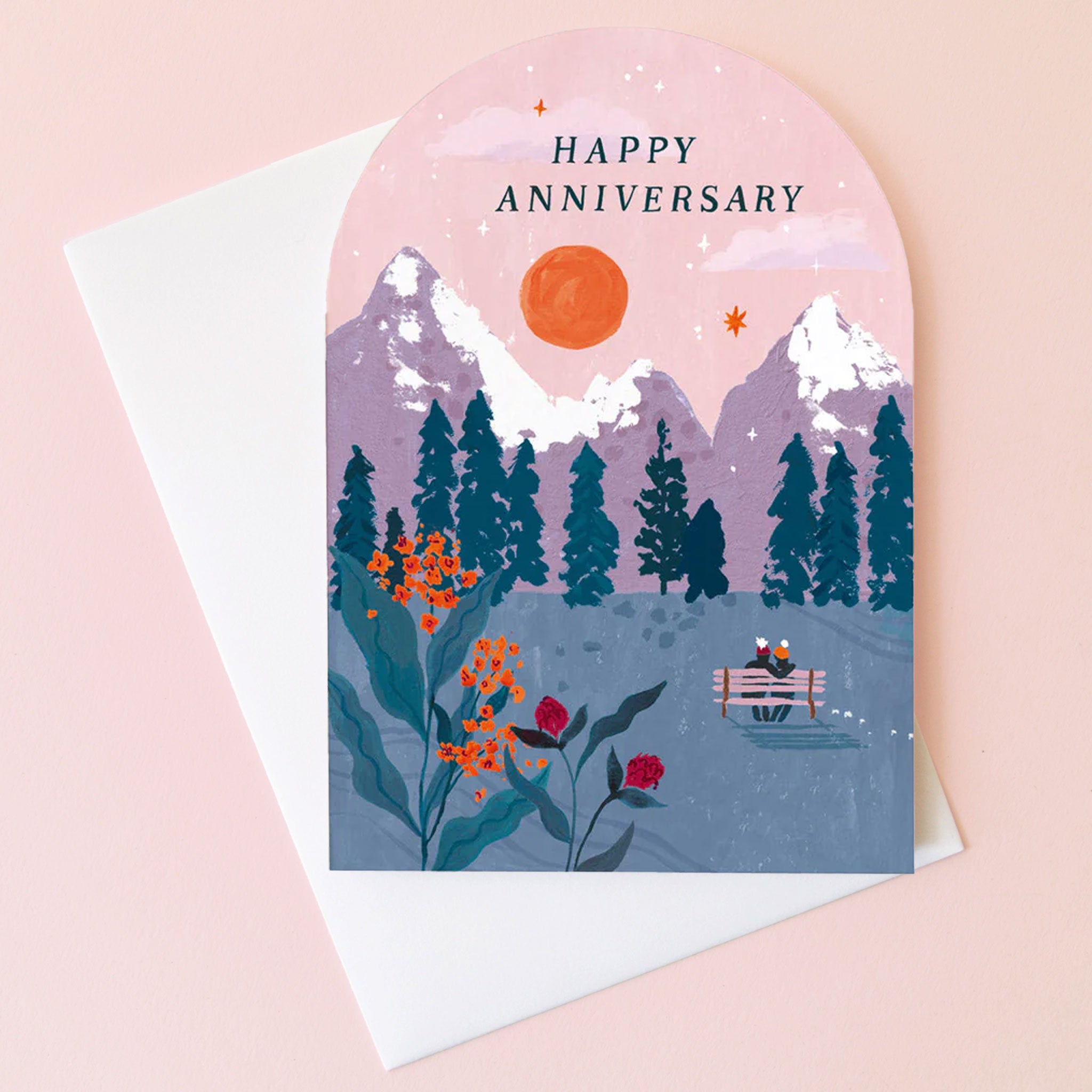 On a pink background is an arched card with a mountainous illustration and text at the top that reads, "Happy Anniversary". 