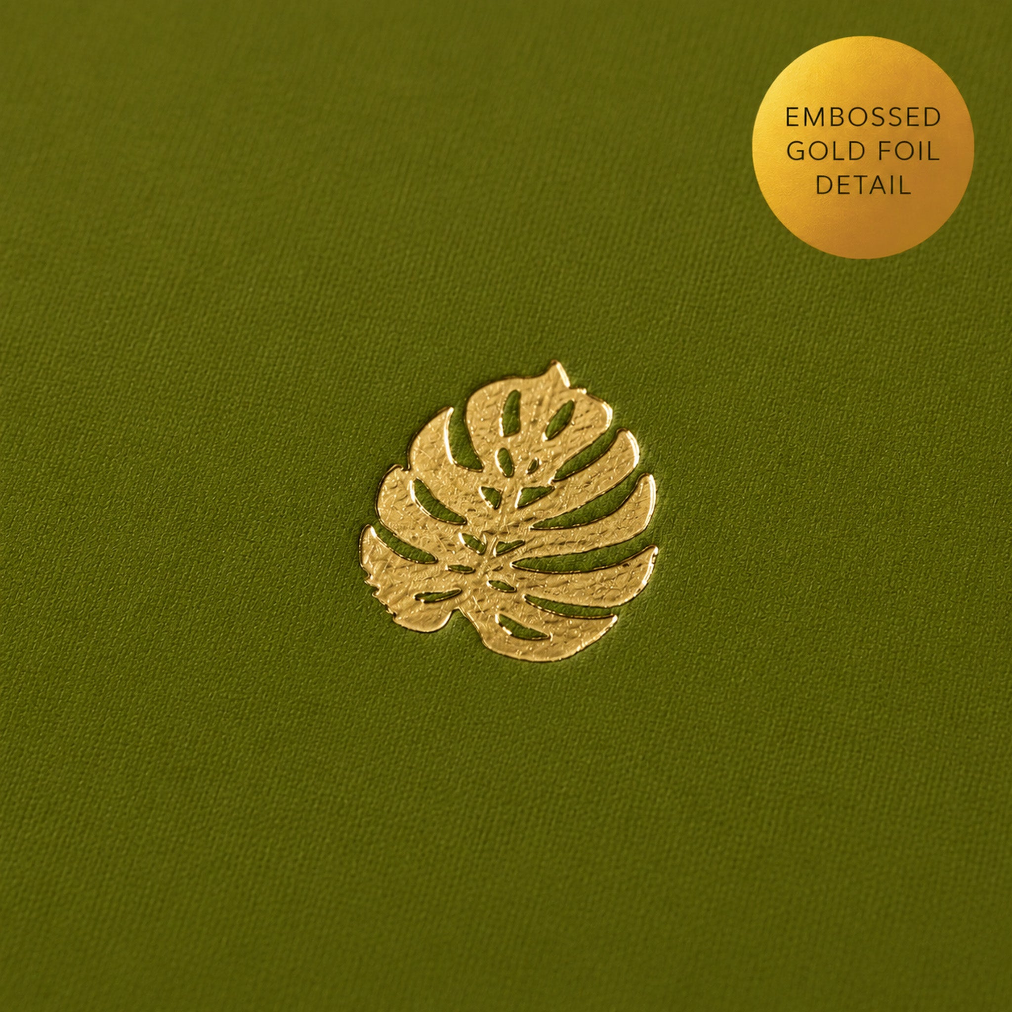 Detail photo of a gold embossed monstera leaf on a green notebook.