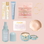 Flat lay of a tropical-themed gift bundle on a blush background, featuring a floral perfume oil, blue lip treatment, pink hair tie bracelet set, gold hoop earrings, lavender barrette clips, sea shell dish, blue hair perfume, pale blue claw clip, and a patterned candle.