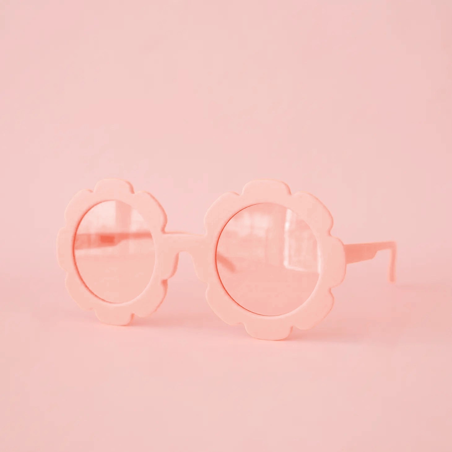On a pink background is a light pink pair of flower shaped sunglasses with a light pink circle lens in the center. 