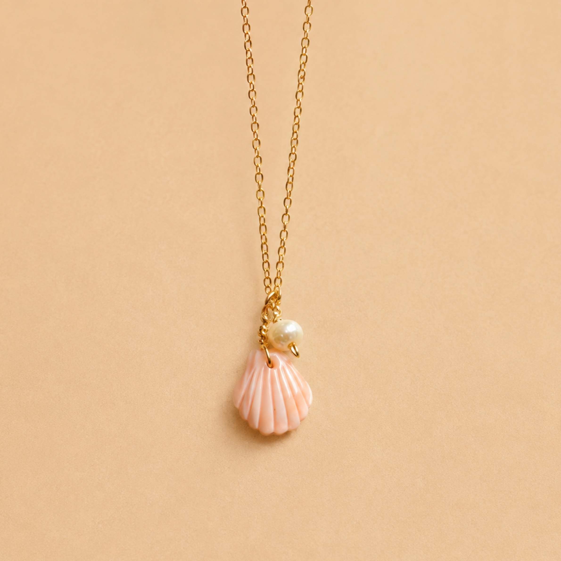 a gold necklace with a pearl and shell shaped pendant. 
