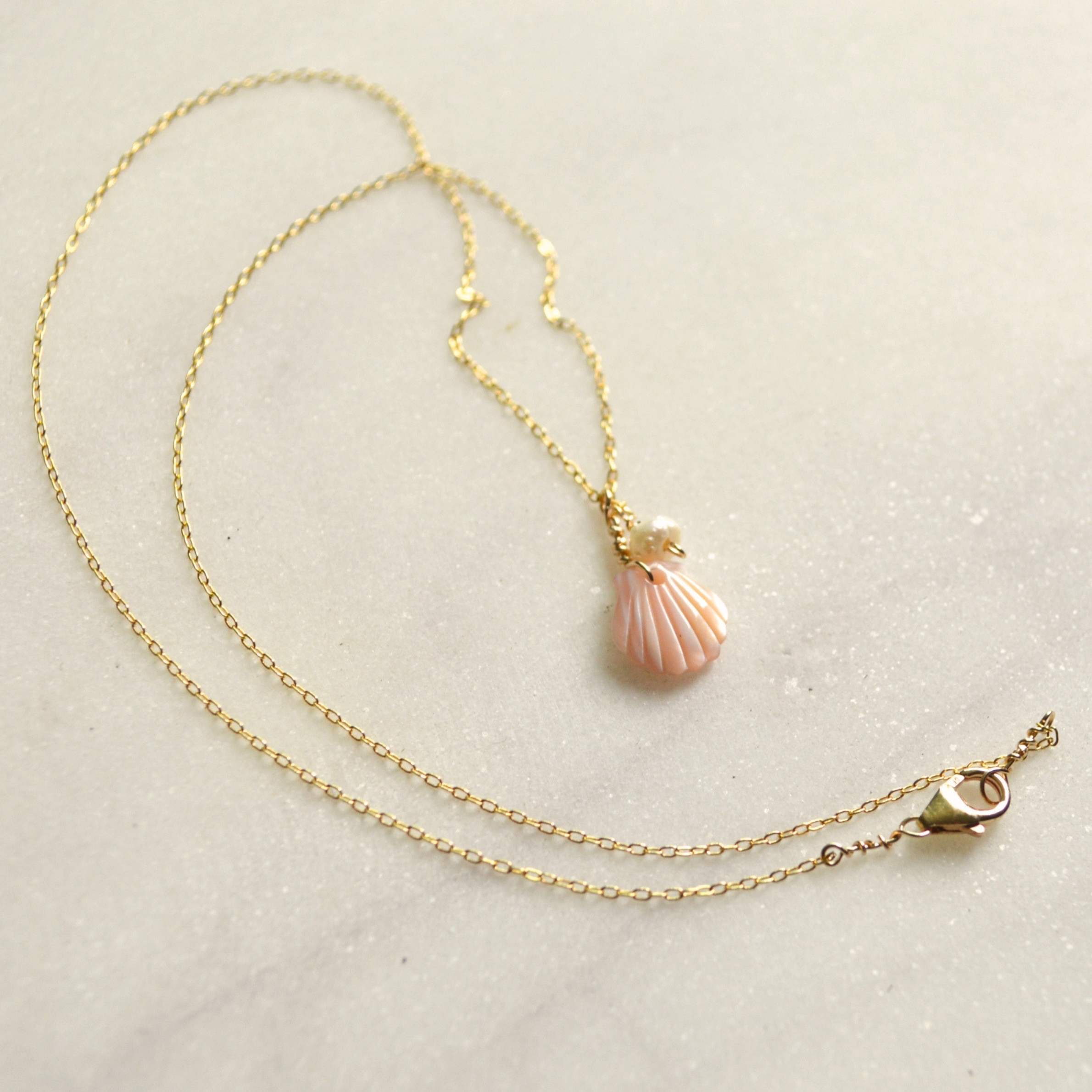 a gold necklace with a pearl and shell shaped pendant. 