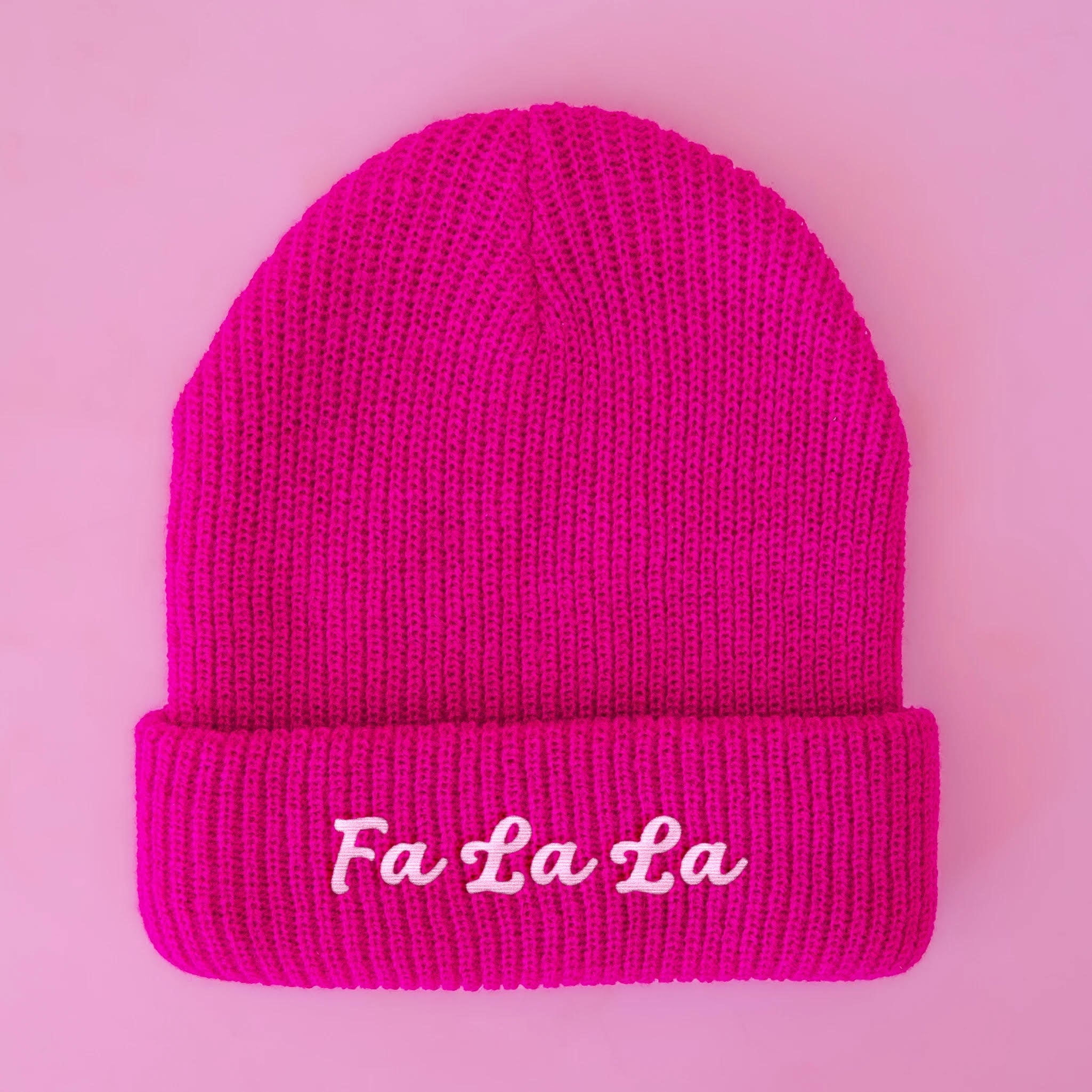 A hot pink beanie with white embroidered text that reads, "Fa La La". 