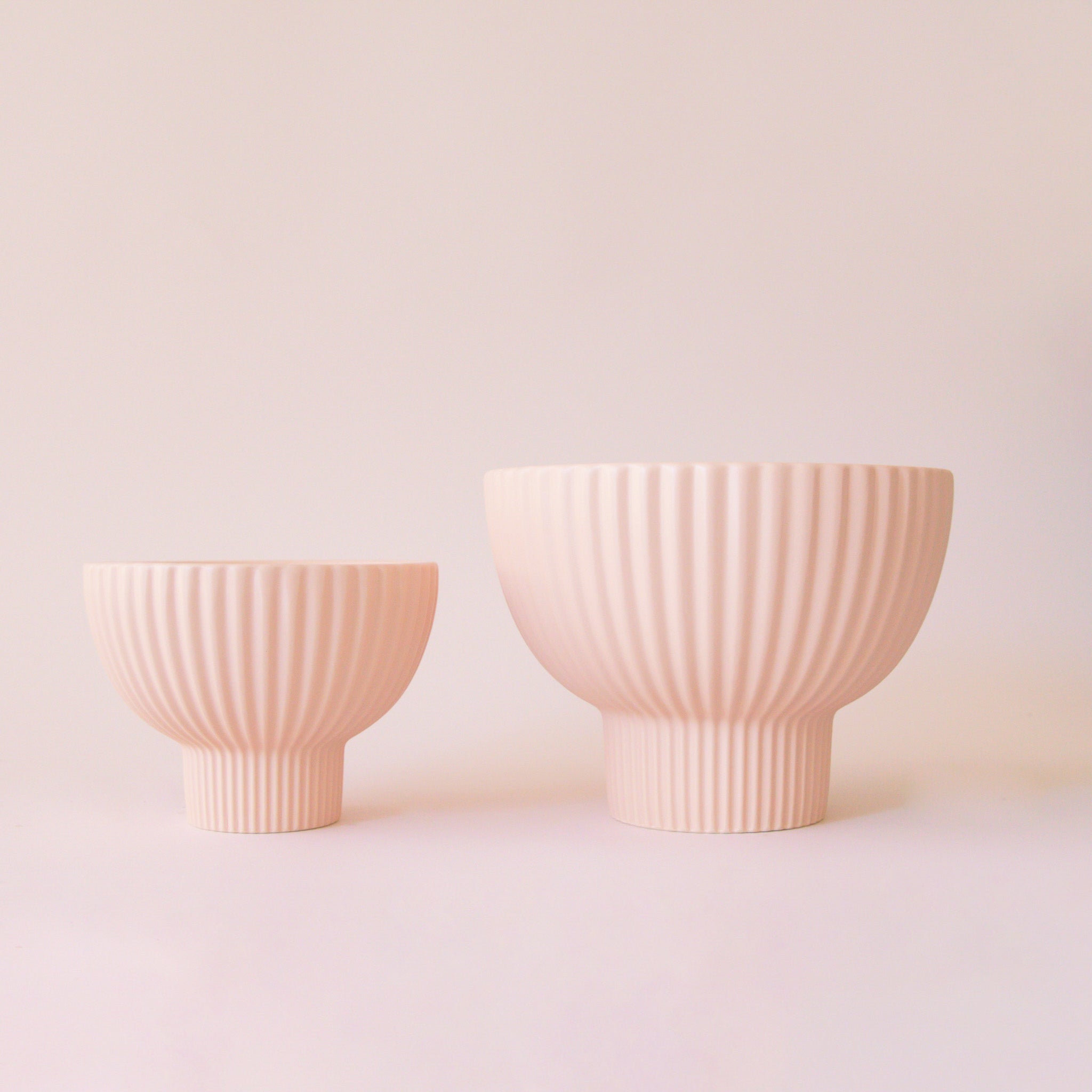 Two pink textured pedestal planter bowls on a light pink background