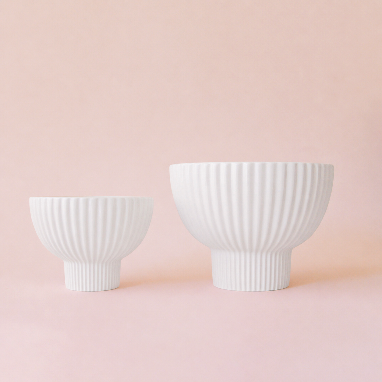 Two white ceramic bowls with textured design on a pink background