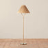 A neutral rattan floor lamp with a brass base, bamboo wrapped post and a woven lampshade. 