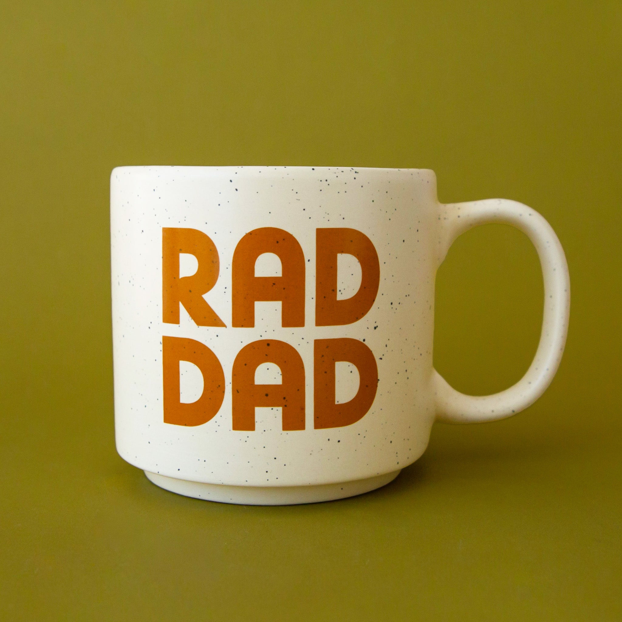 A ceramic speckled mug with printed text on the front that reads, "RAD DAD". 