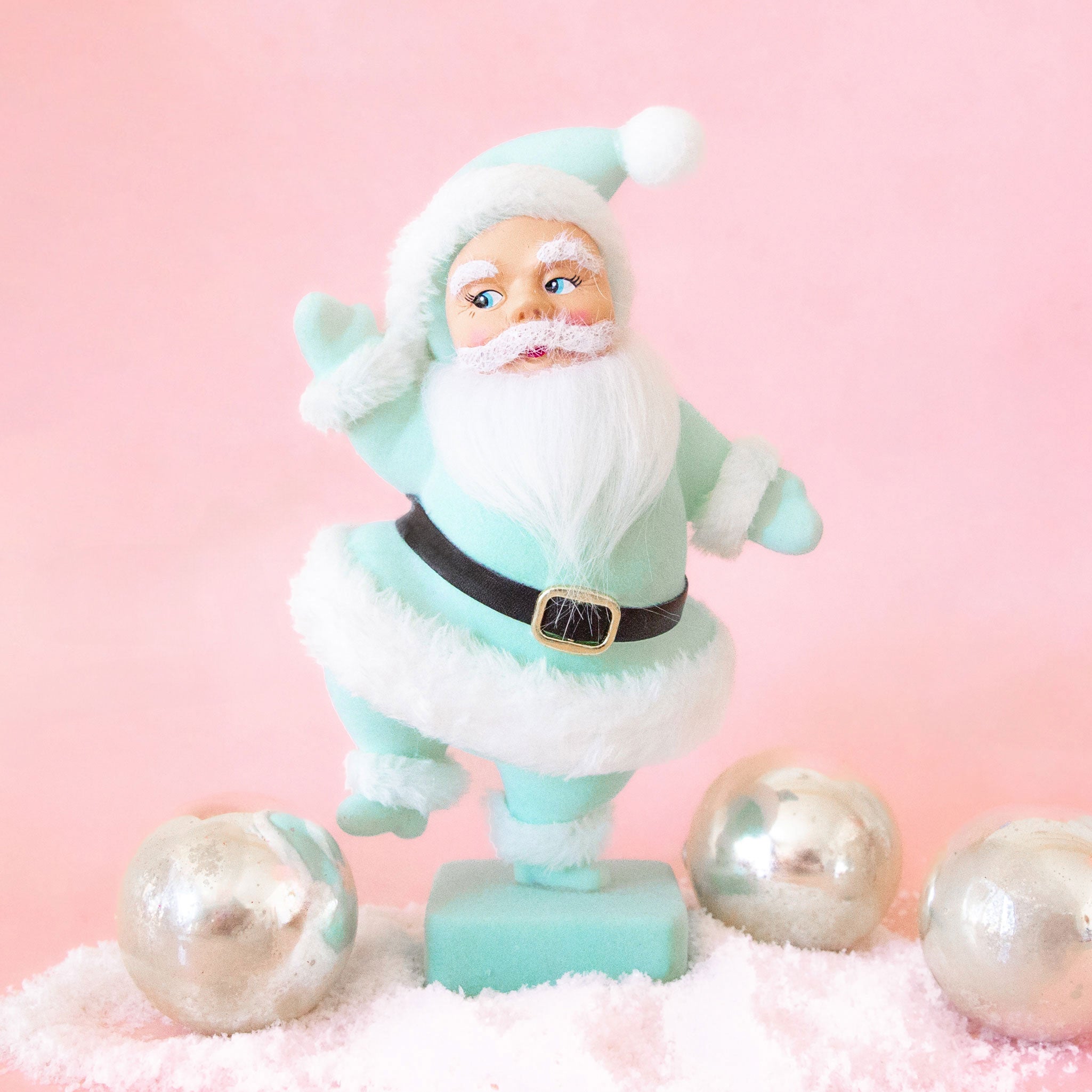On a pink background is a Santa figurine wearing a mint colored suit with the fluffy details. 