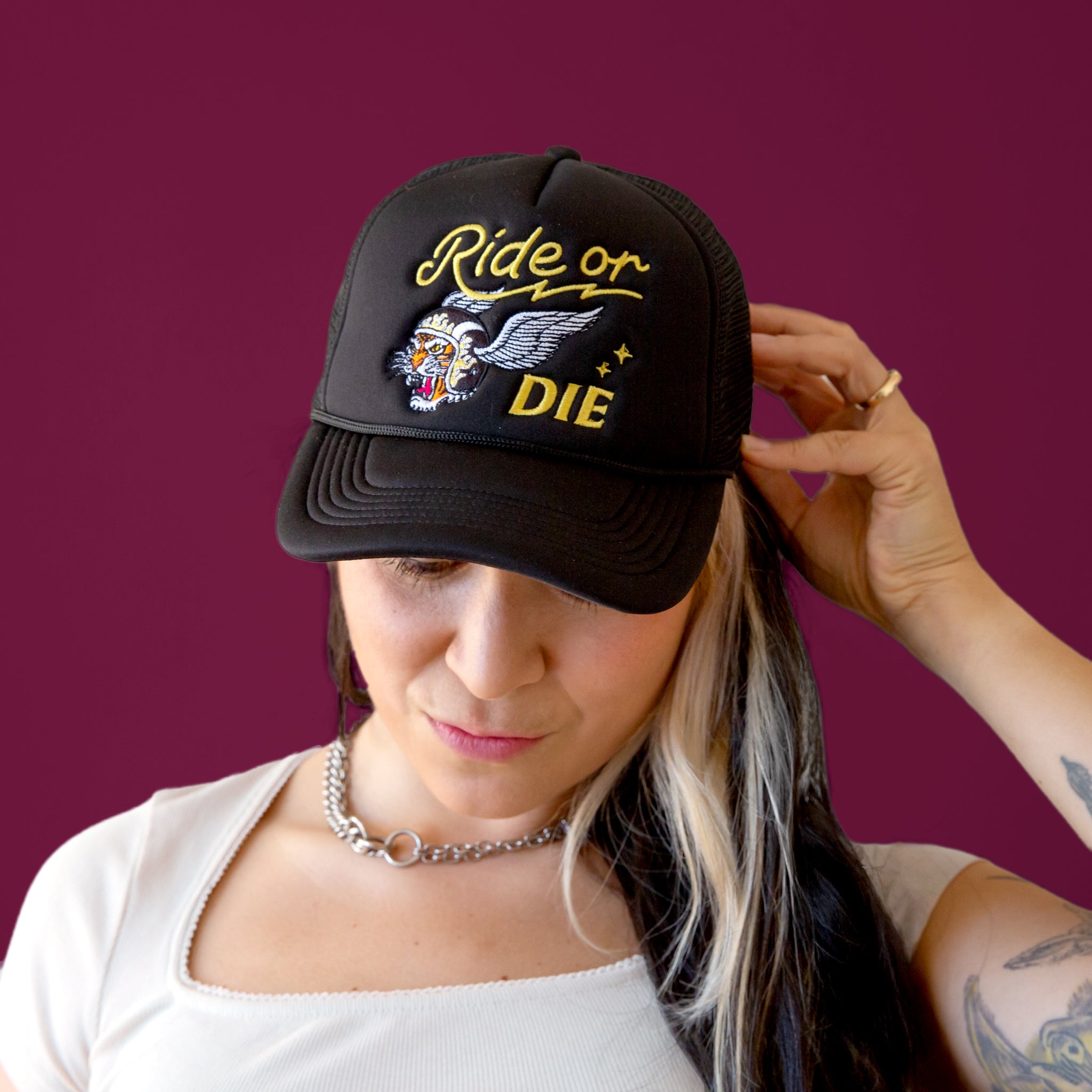 Model wearing a black trucker hat that reads " Ride or Die".