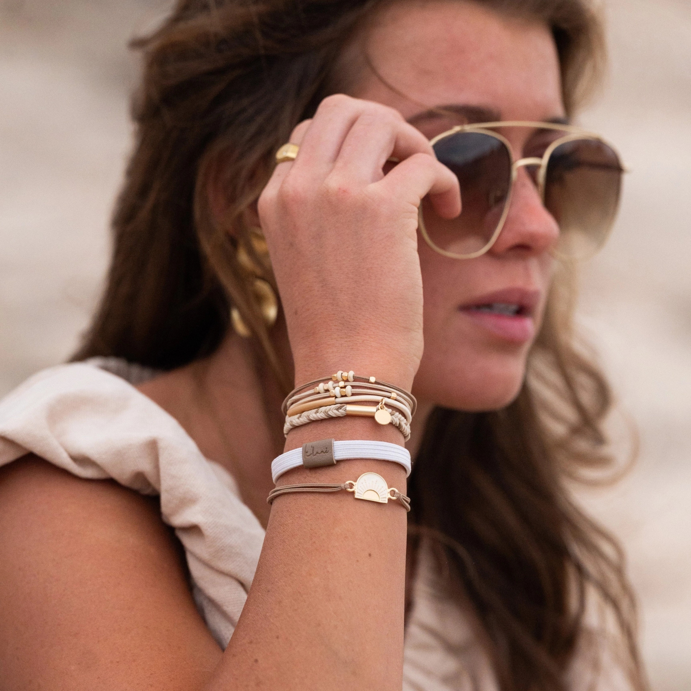 A set of five bohemian-style hair ties and bracelets displayed on a beige backing card. The set includes braided elastic bands, thin brown cords, a gold-tone sun charm, and small bead accents.