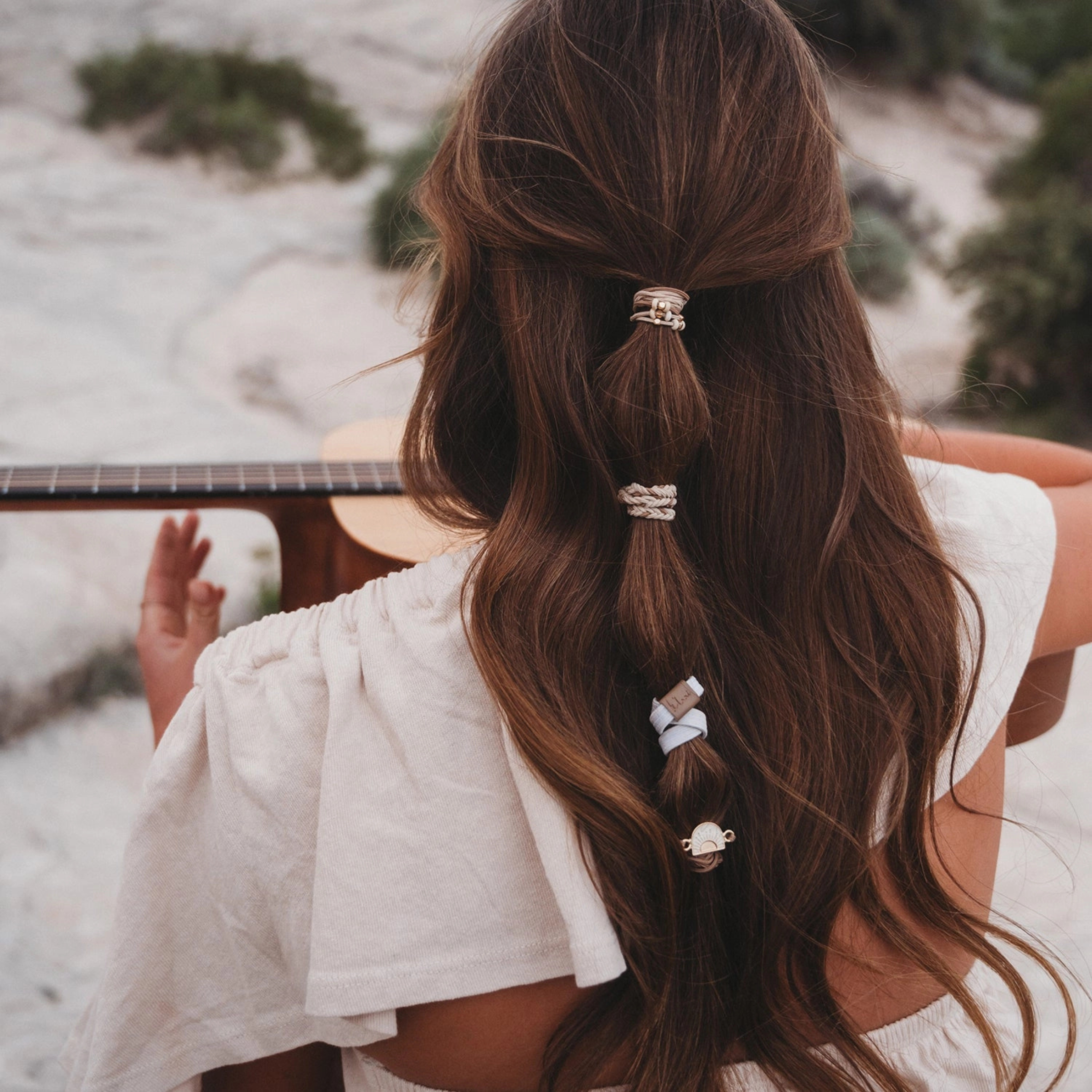 A set of five bohemian-style hair ties and bracelets displayed on a beige backing card. The set includes braided elastic bands, thin brown cords, a gold-tone sun charm, and small bead accents.