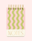 On a white background is a pink and green wavy line notebook with a gold spiral binding and text at the bottom that reads, "NOTES". 