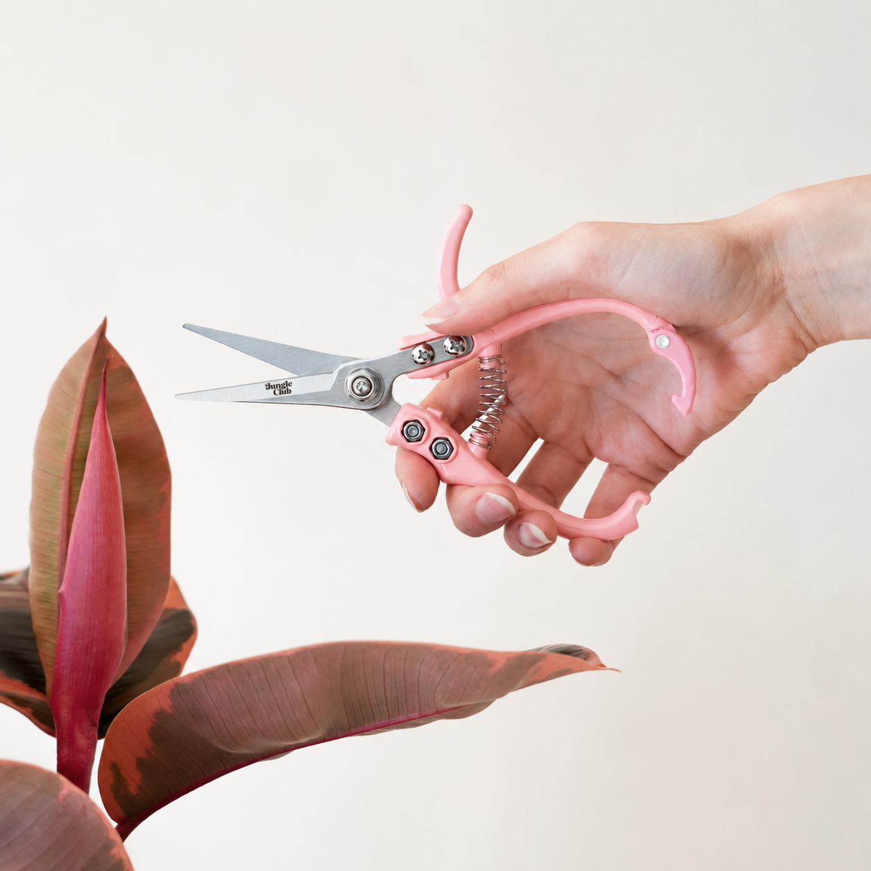 The pink pruning shears in action staged next to a plant. 