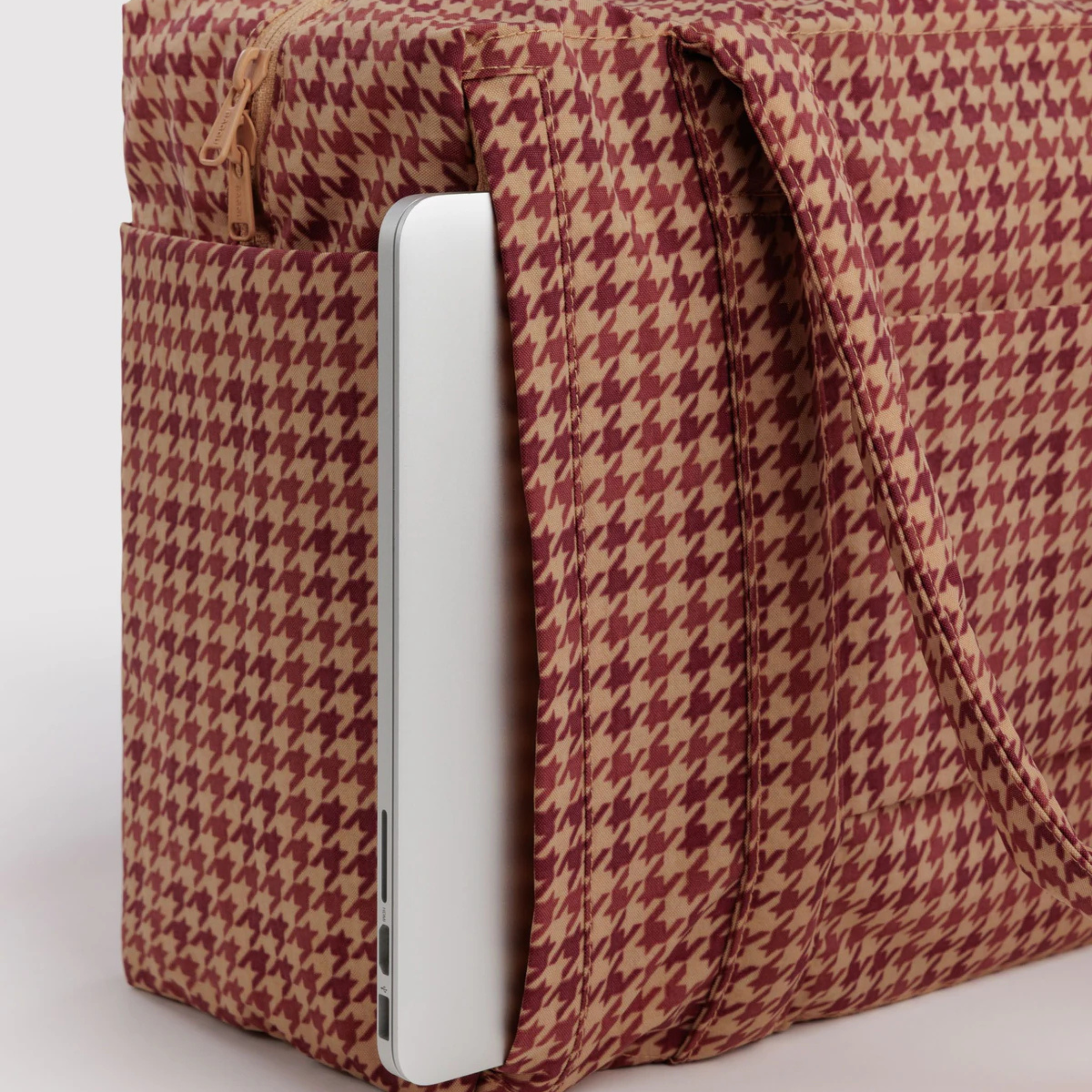 A tan and rust colored printed nylon carry on bag.