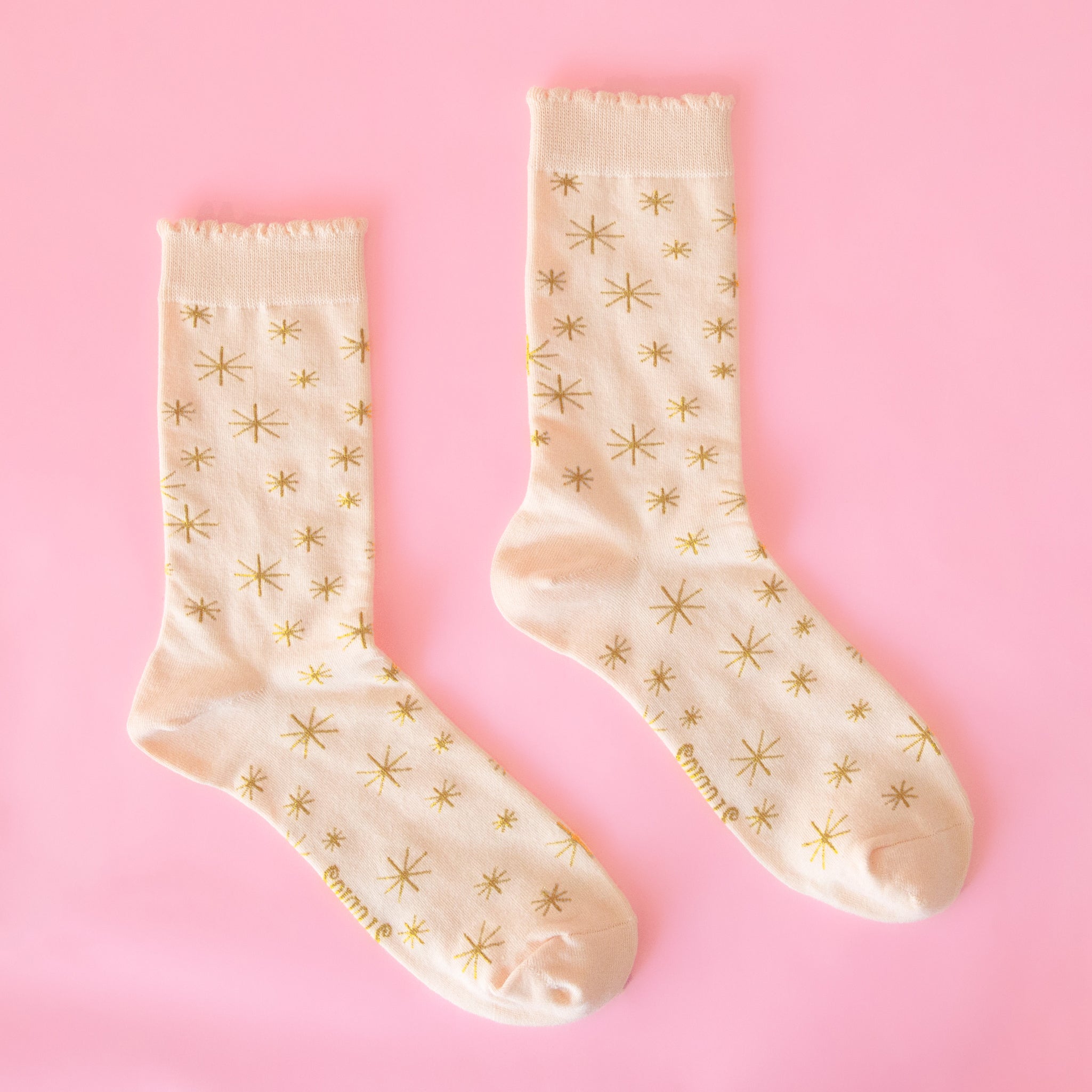 A pair of cream colored socks with a gold star pattern. 