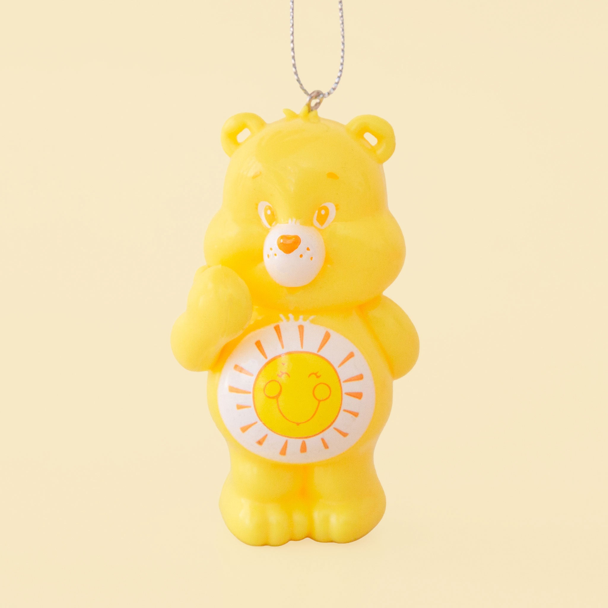 A yellow care bear shaped ornament with a yellow and orange smiling sun graphic on its stomach. 