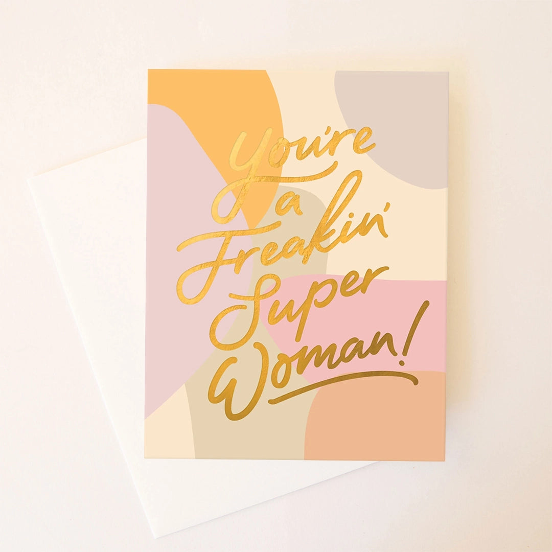 On a white background is a multicolored card that reads, &quot;You&#39;re a Freakin&#39; Super Woman!&quot; in gold text. 