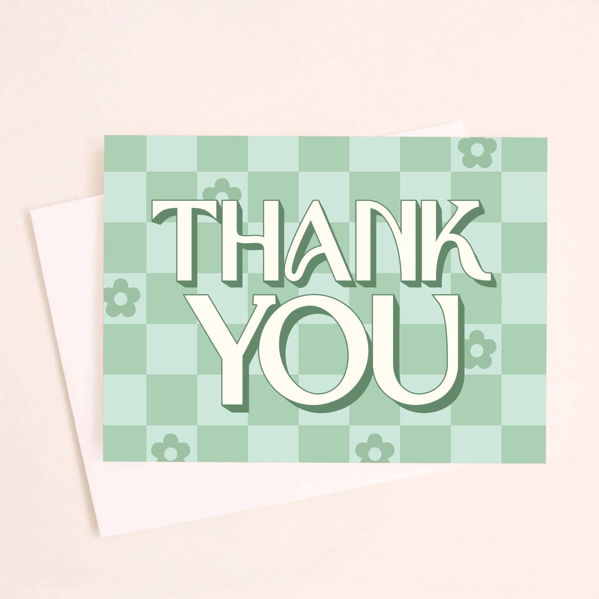 On a white background is a green checker print greeting card that reads, &quot;Thank You&quot; along with scattered daisies in some of the squares.