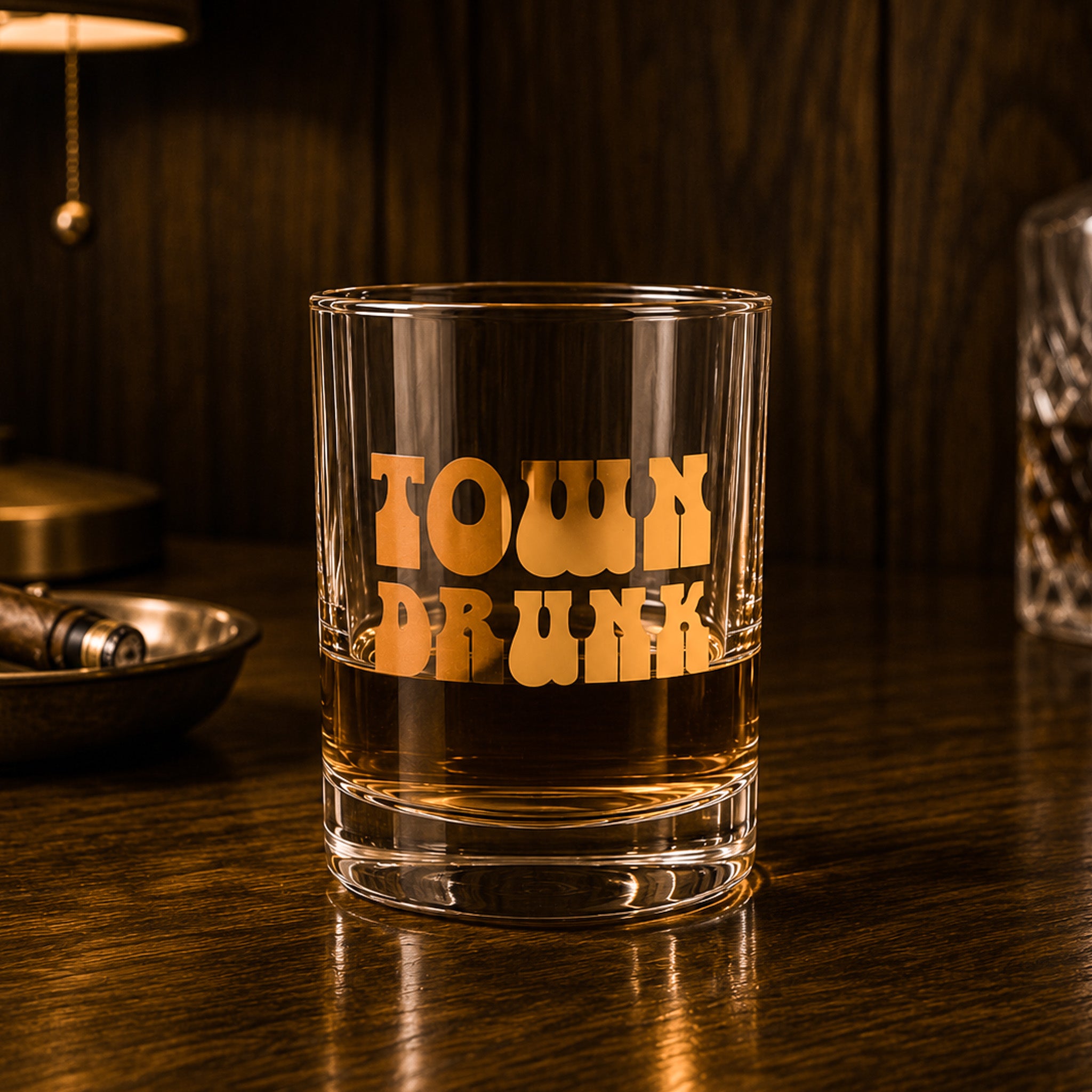 A clear glass tumbler with gold foiled text that reads, "Town Drunk". 