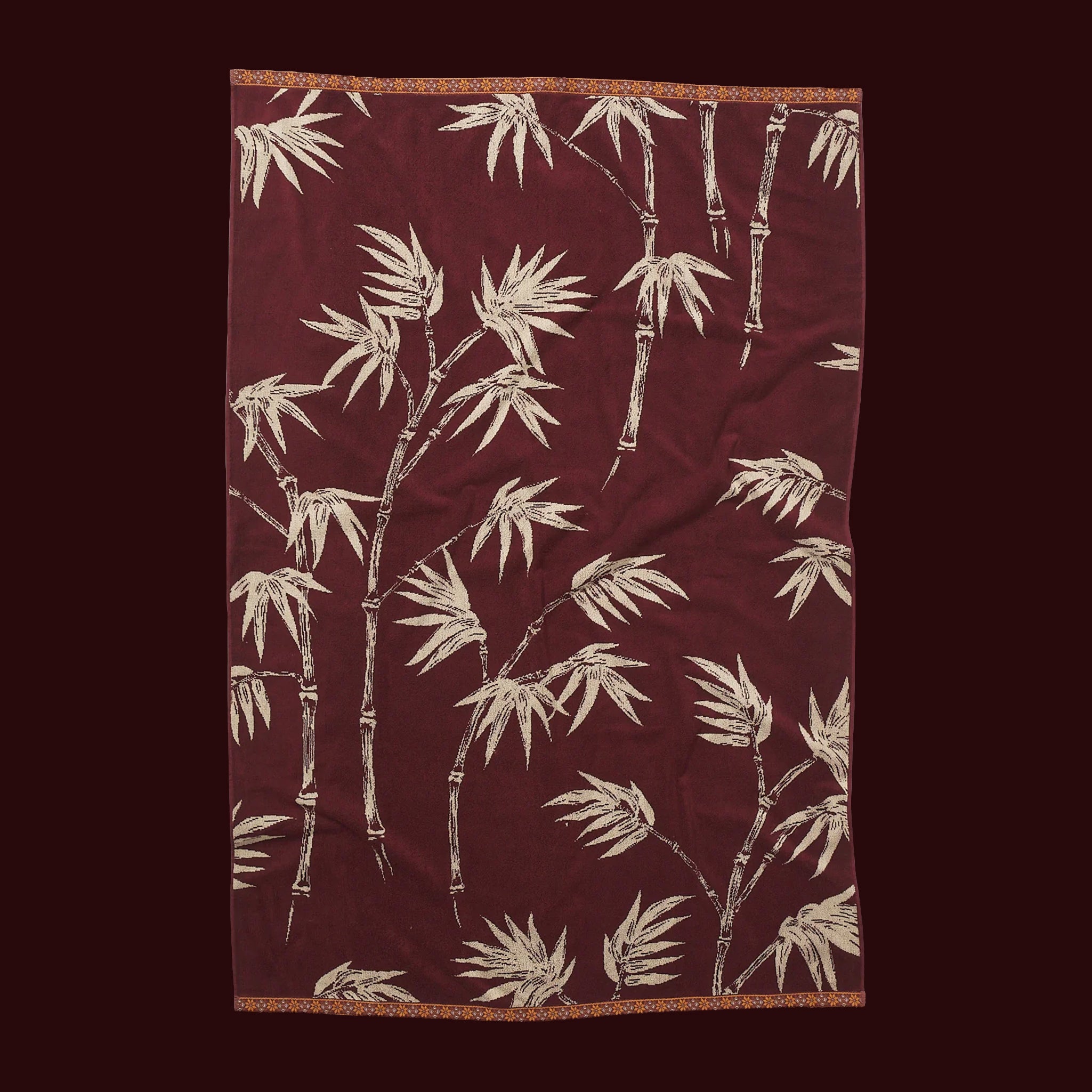 Burgundy towel with a cream bamboo leaf pattern laid flat against a dark background.