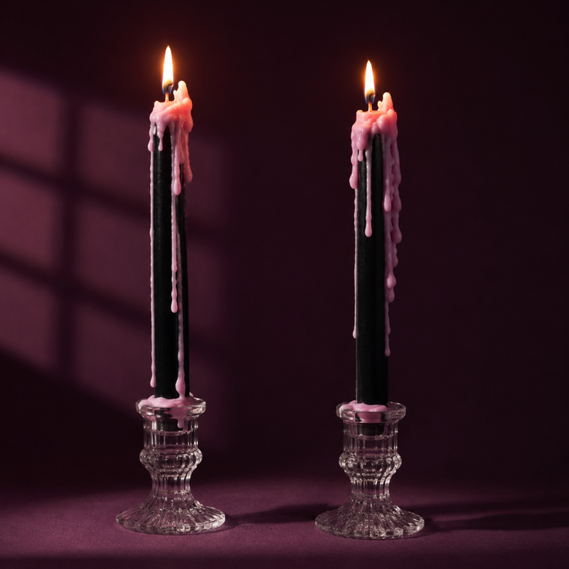 Two tall black taper candles with pink wax dripping down, set in clear glass candle holders against a dark purple background.