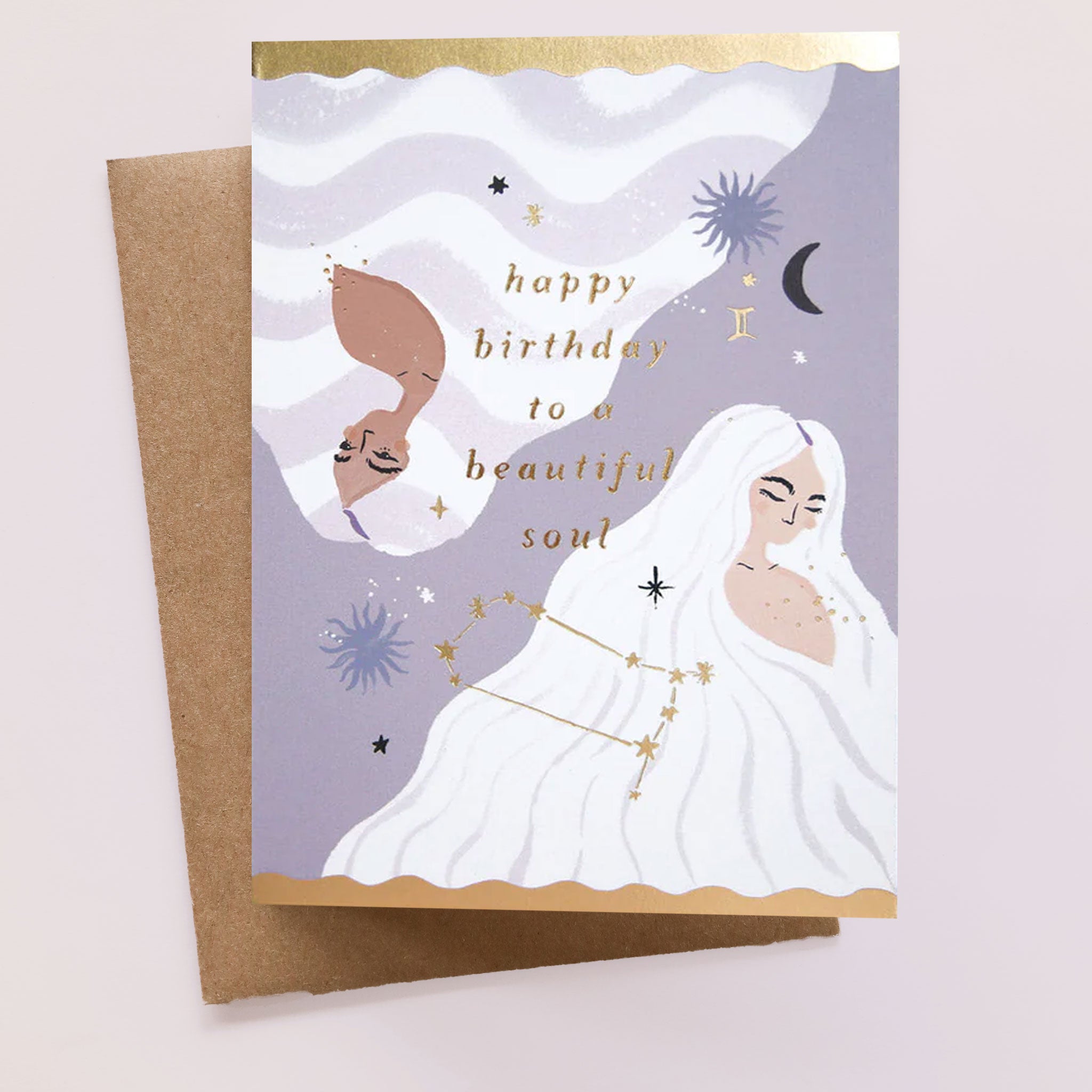 On a neutral background is a card with a woman on the front and gold text that reads, &quot;happy birthday to a beautiful soul&quot; along with star and moon illustrations. 