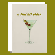 a white card with a martini graphic on the front and text above that reads, "a tini bit older". 