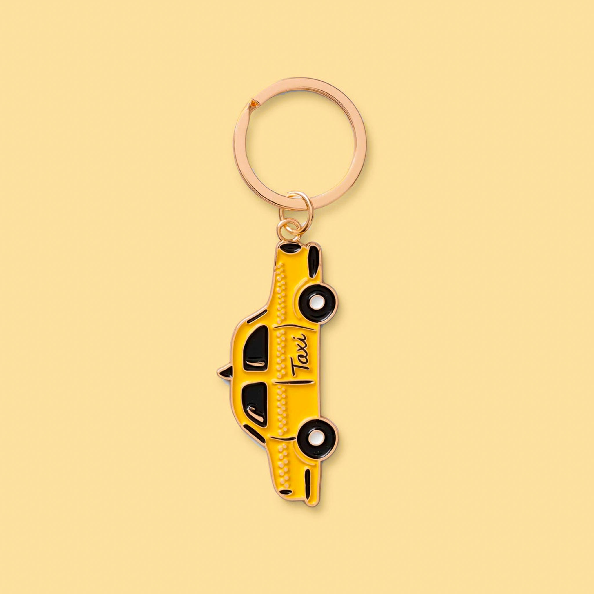A gold keychain that looks like a New York taxi hangs from a brass ring.  The taxi is yellow with black wheels and windows. The tires have a white circle in the middle.  The background is a soft yellow color.