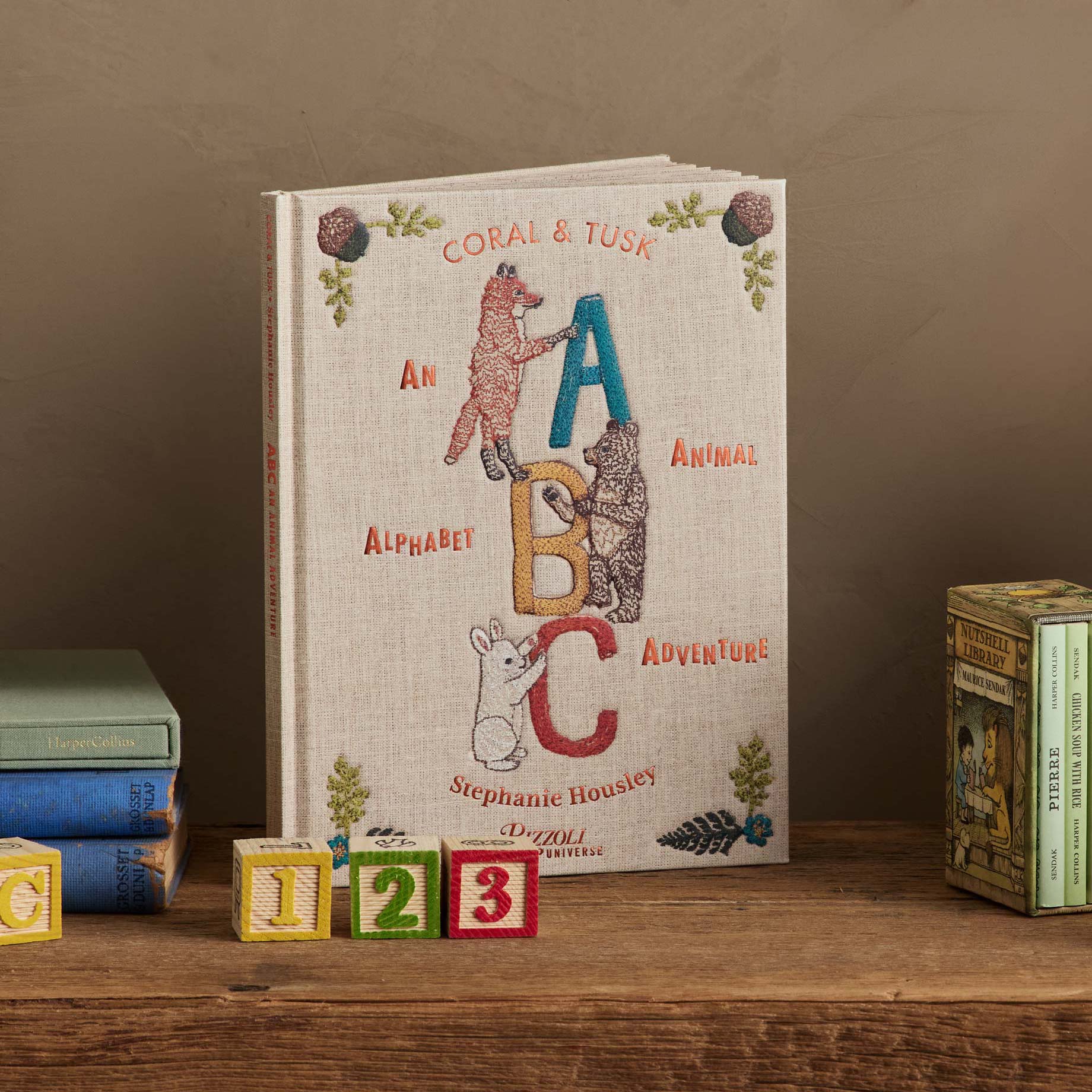 Cover of the children’s book ABC: An Animal Alphabet Adventure by Stephanie Housley displayed upright on a wooden table with toy number blocks and books.